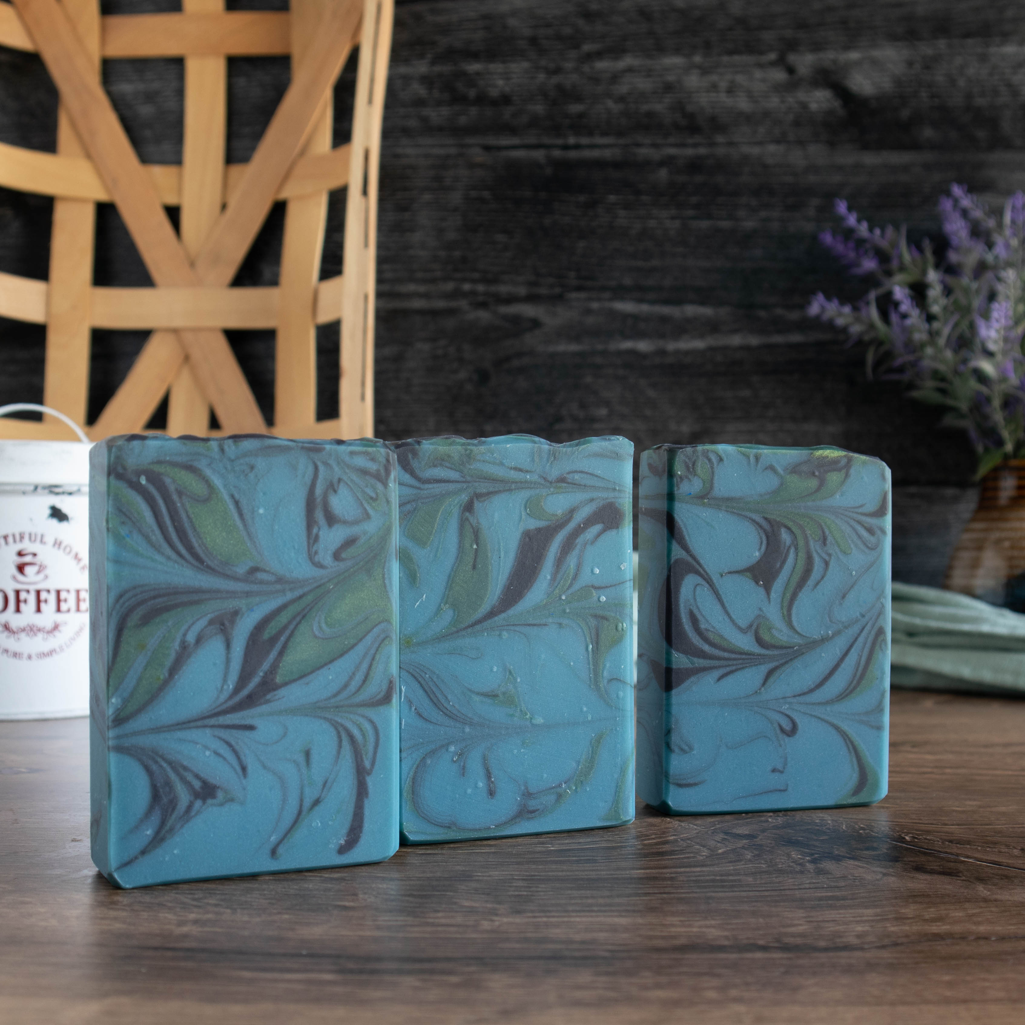 3 bars of southern gentleman are standing in a row. they are showing the main blue color with swirls of black and green. they are sitting on a walnut wood board with a black wooden background.