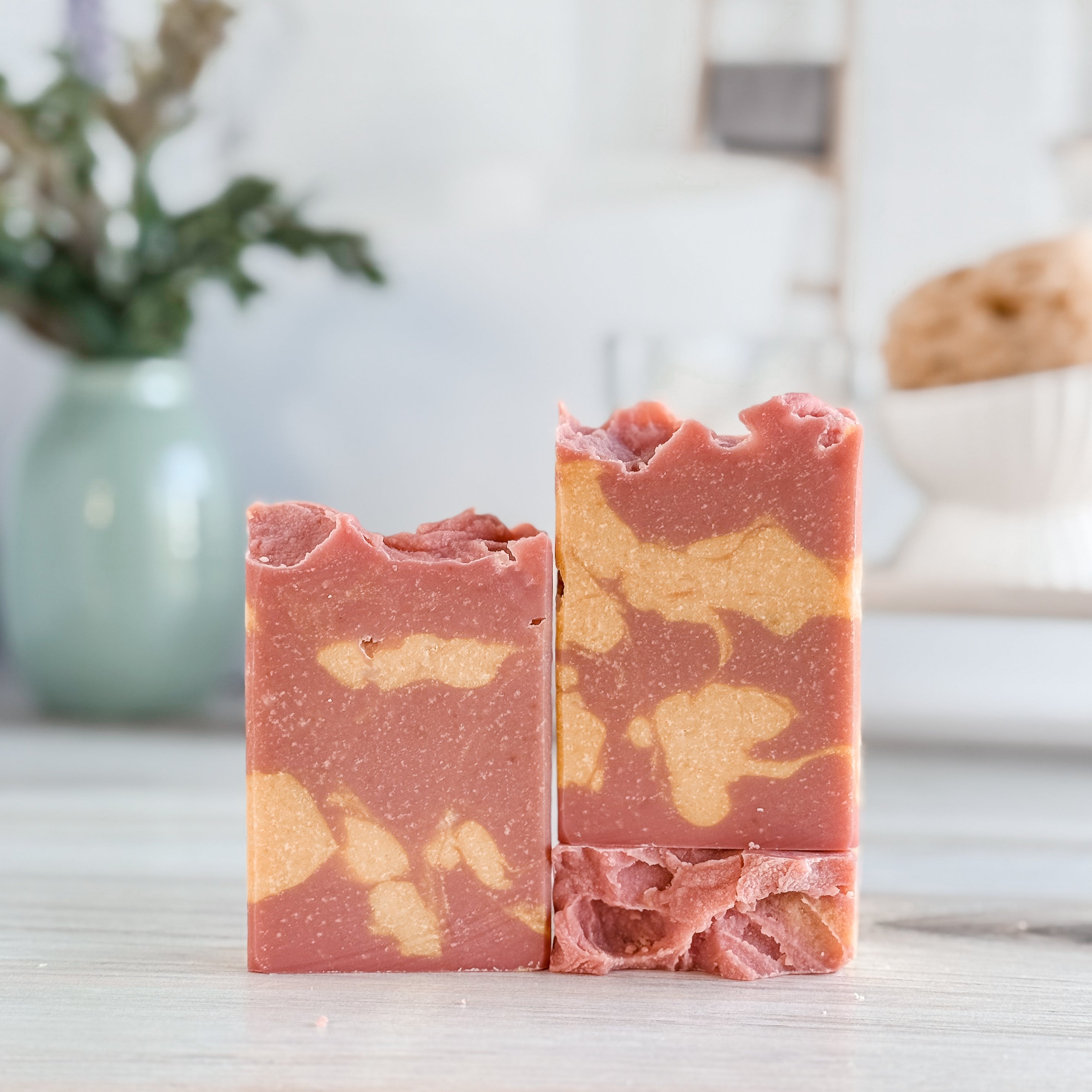 Three bars of pink and orange marbled soap on a light surface with a blurred background