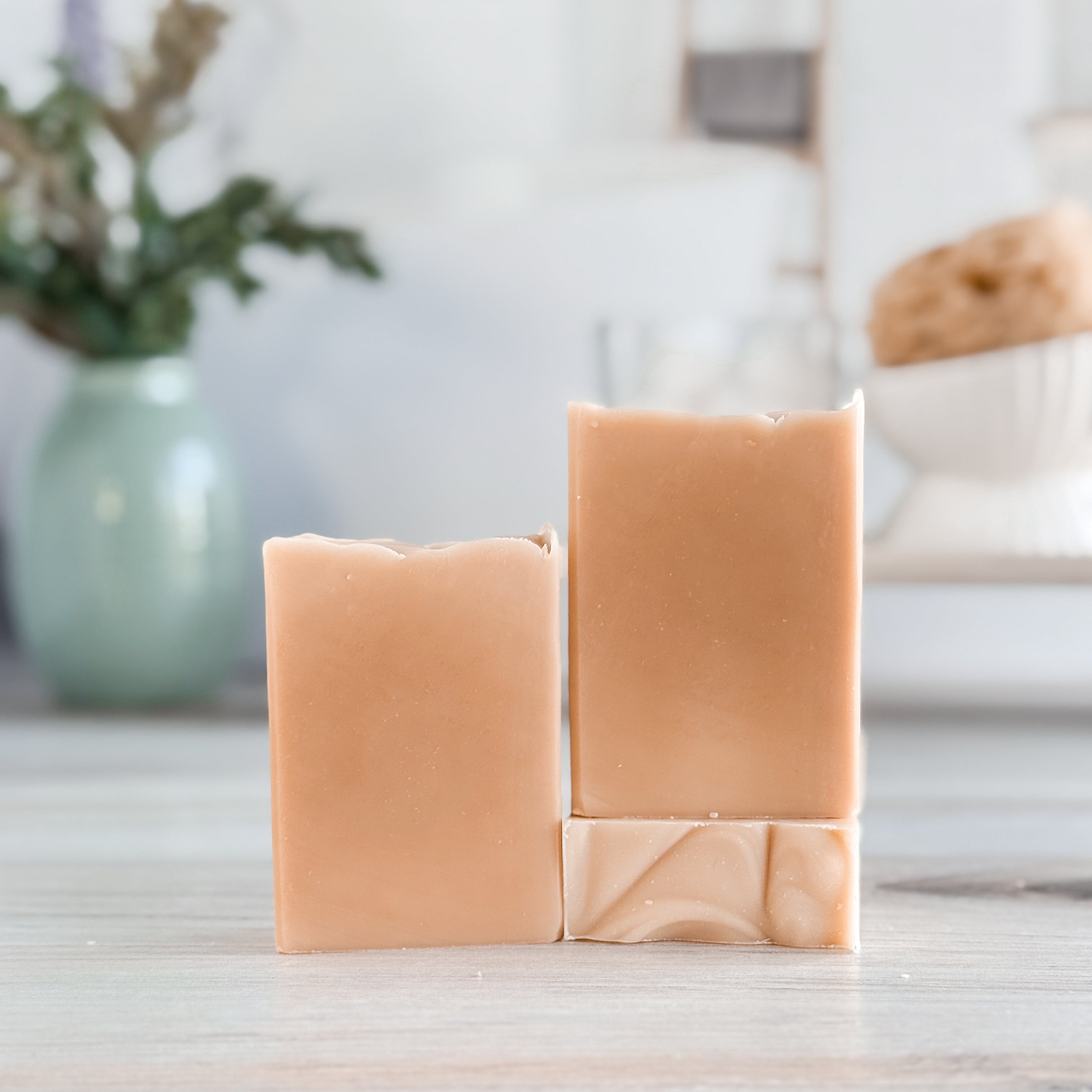 Three bars of soap stacked on a wooden surface with a blurred background