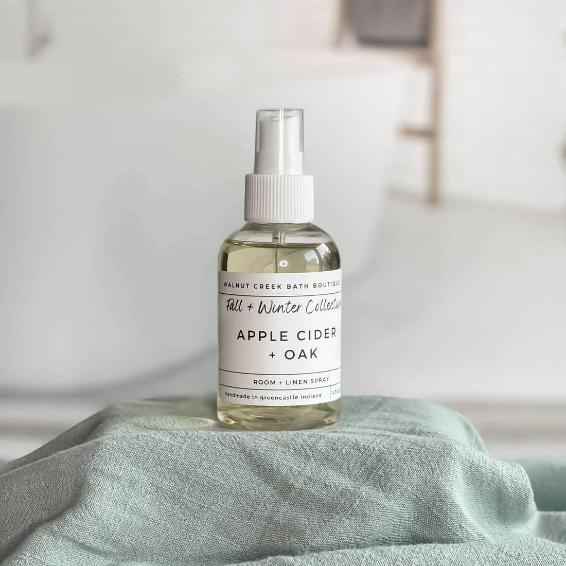 Bottle of Apple Cider + Oak room spray on a green fabric surface with a neutral background