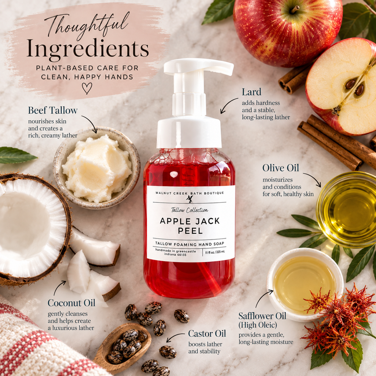 A bottle of Rainforest Bath Boutique Tallow Collection Apple Jack Peel Tallow Foaming Hand Soap is centered on a marble surface surrounded by ingredient callouts and props including sliced red apples, coconut, castor oil, safflower oil, beef tallow, and cinnamon sticks.