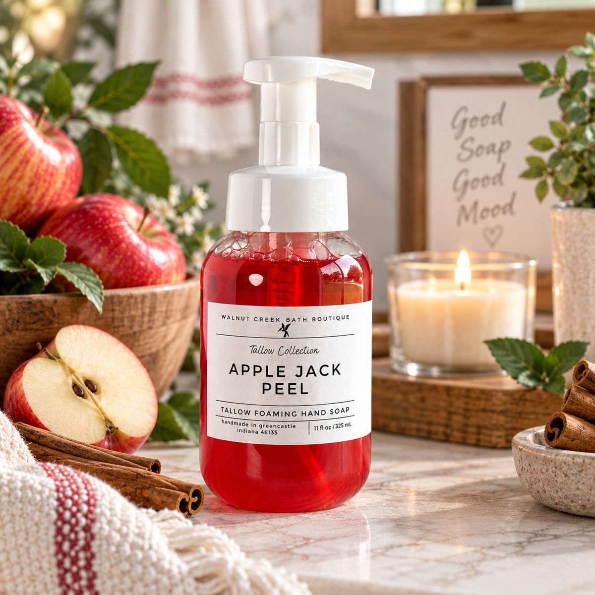 A bottle of Tallow Collection Apple Jack Peel hand soap stands on a marble surface in a styled bathroom scene. The soap liquid is bright red, and the pump is white.