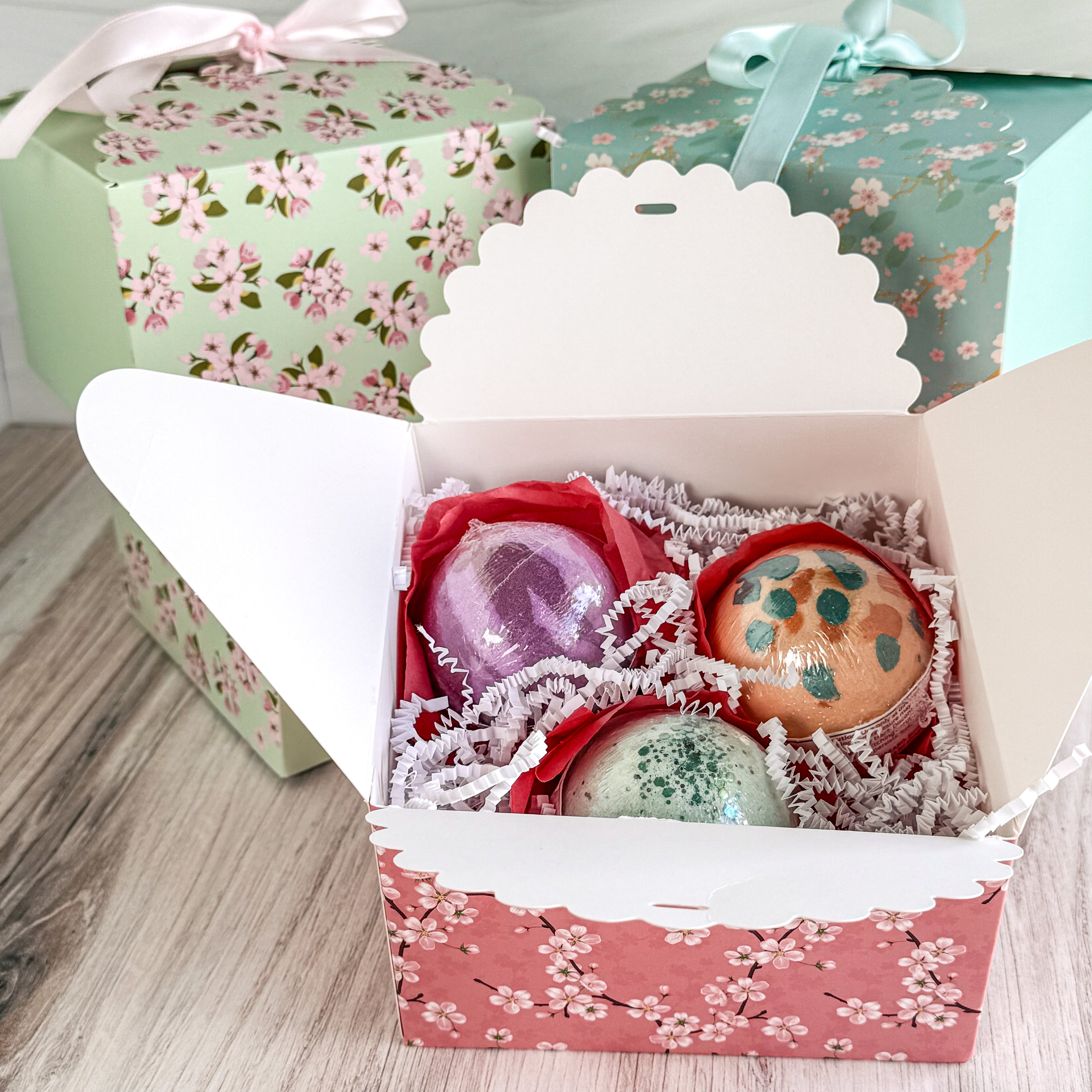 Decorative bath bombs in a floral box with additional boxes in the background.