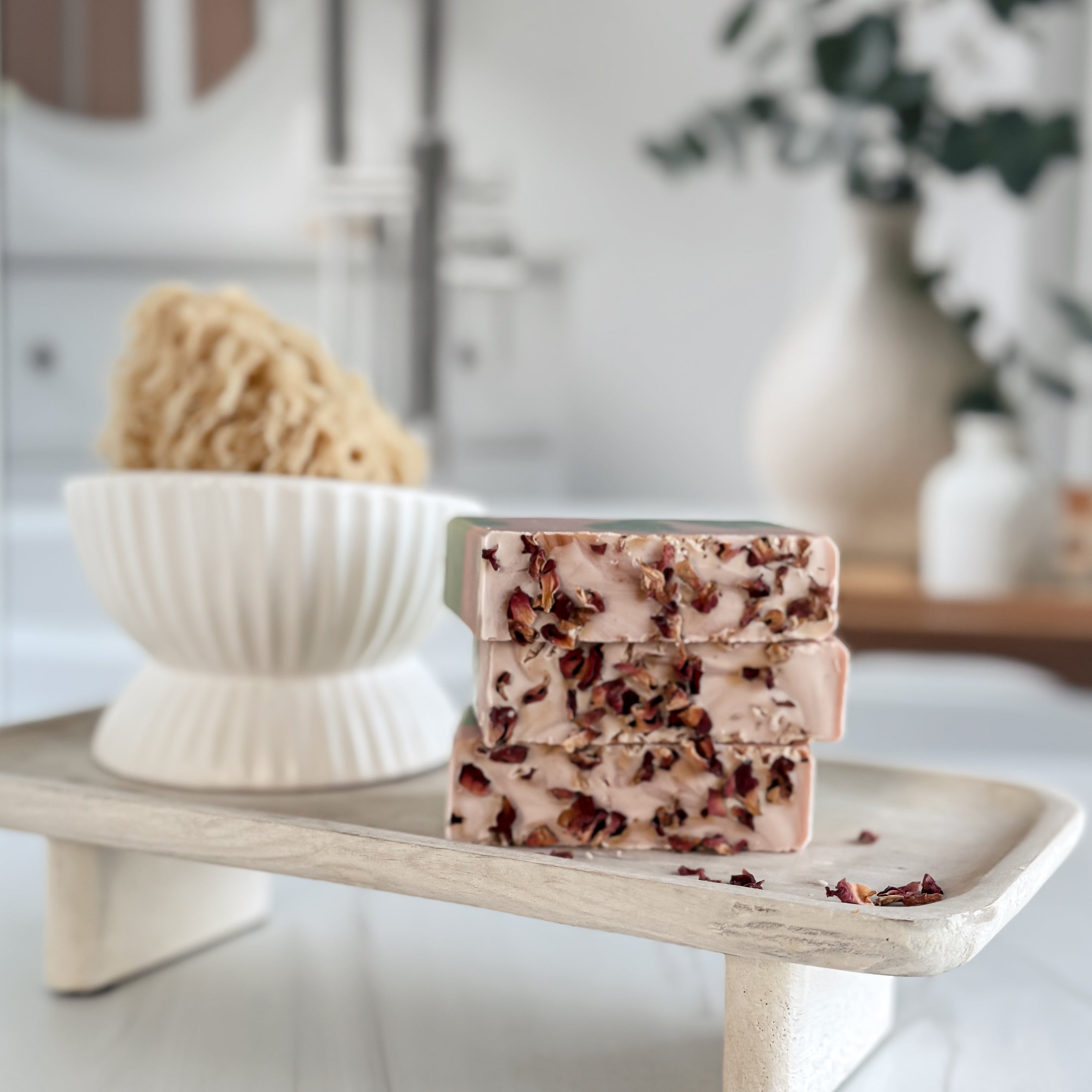 Stack of soap bars with natural ingredients on a wooden stand in a bathroom setting.