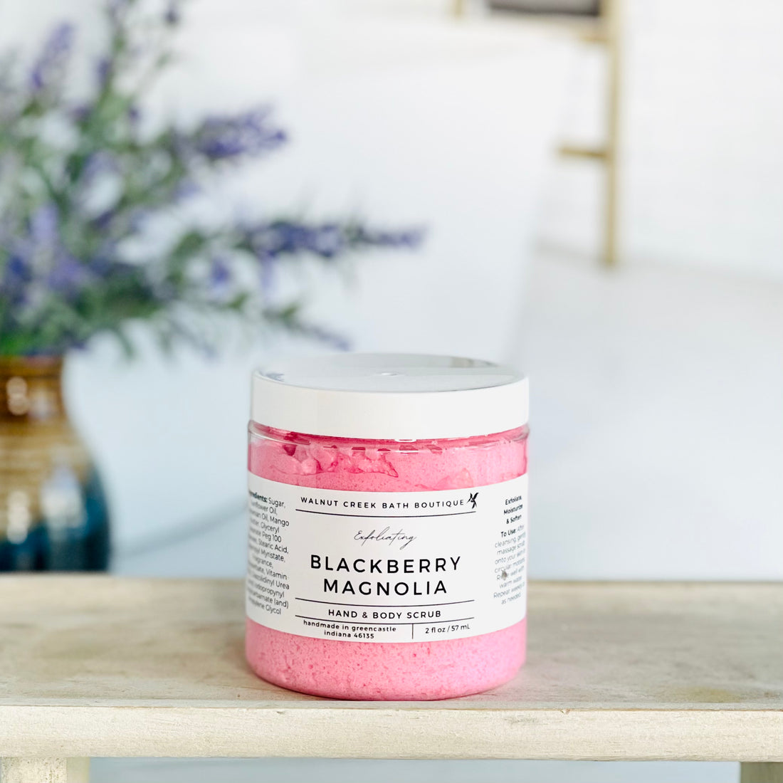 blackberry magnolia scrub is shown on a tray. there is some lavender in the background to give interest to this very calm and neutral image to evoke a peaceful experience.