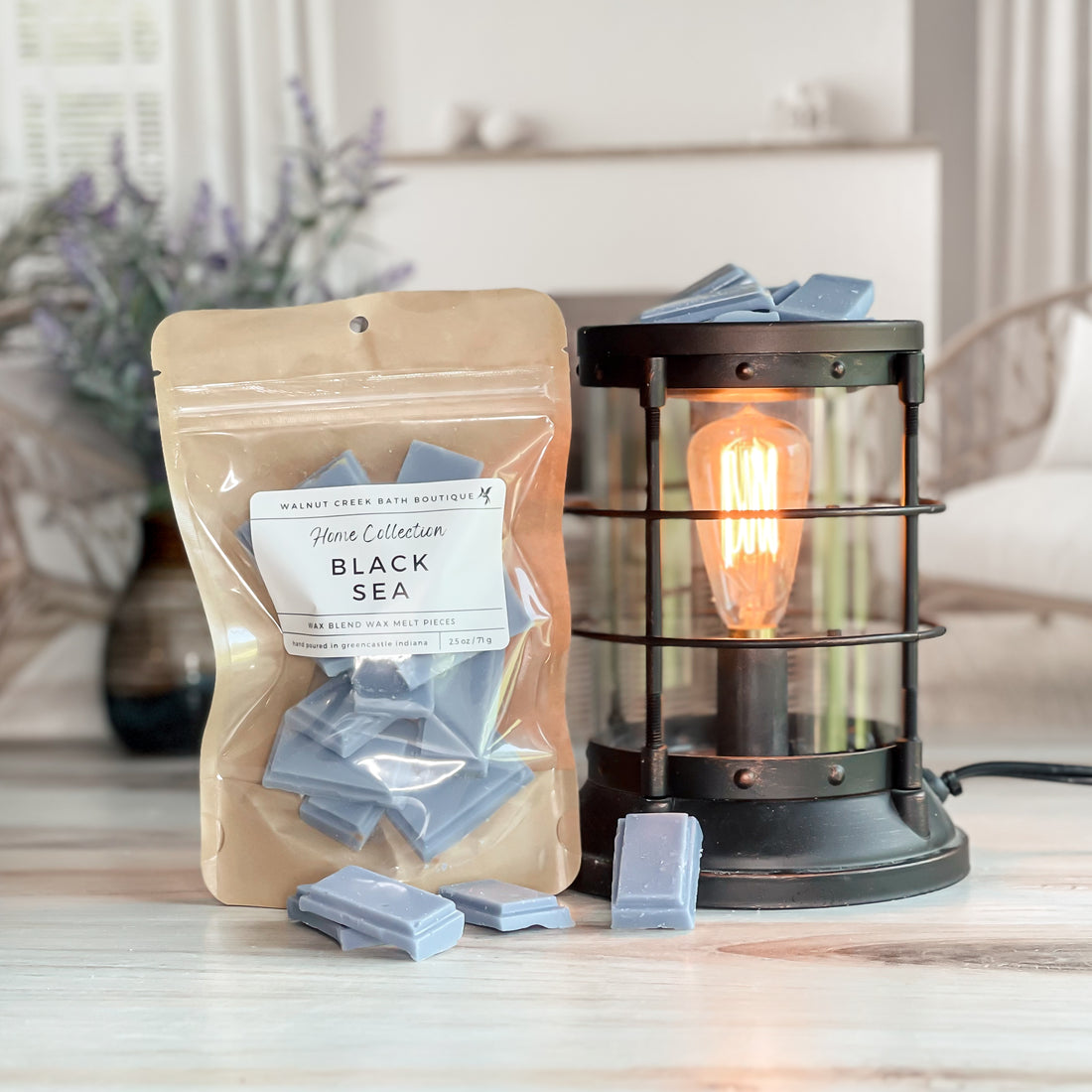 black sea wax melt bag next to lit burner. there are wax melts on the table scattered about to shoe the pieces - these are blue grey candy bar pieces