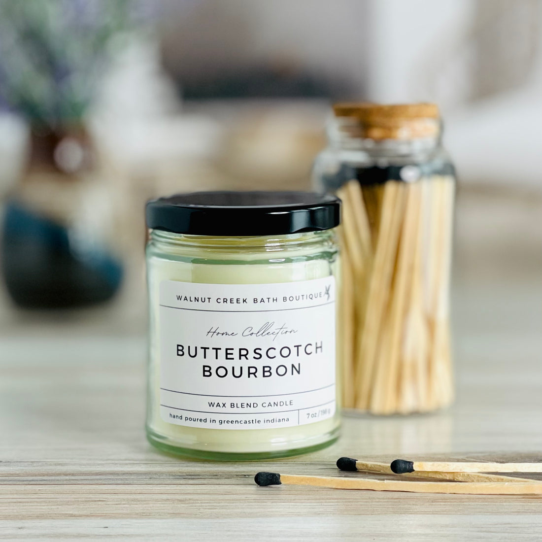 butterscotch bourbon candle with black lid. there are a few matches scattered in front and a pretty glass jar of matches in the background