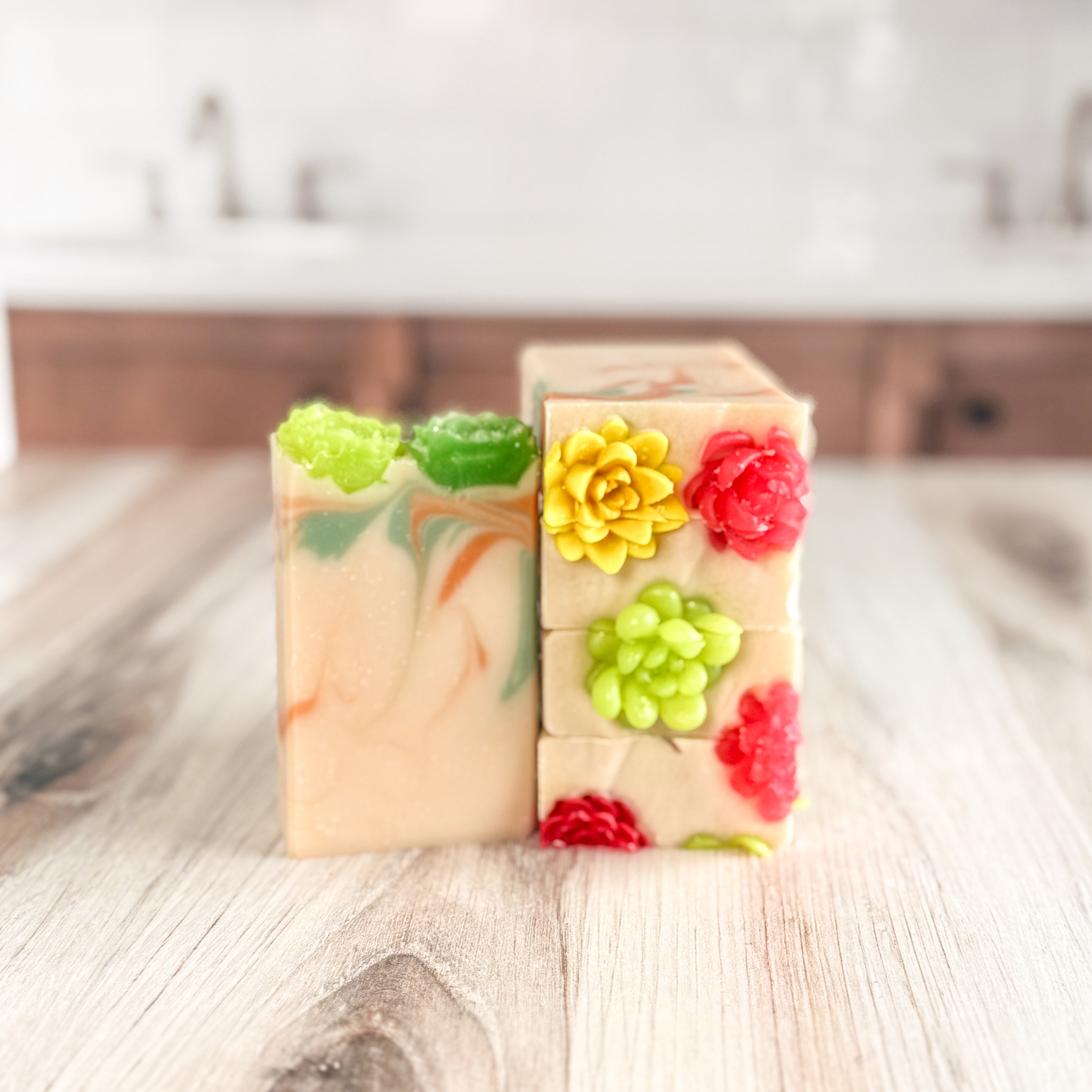 Two handmade soap bars with colorful flower decorations on a wooden surface.