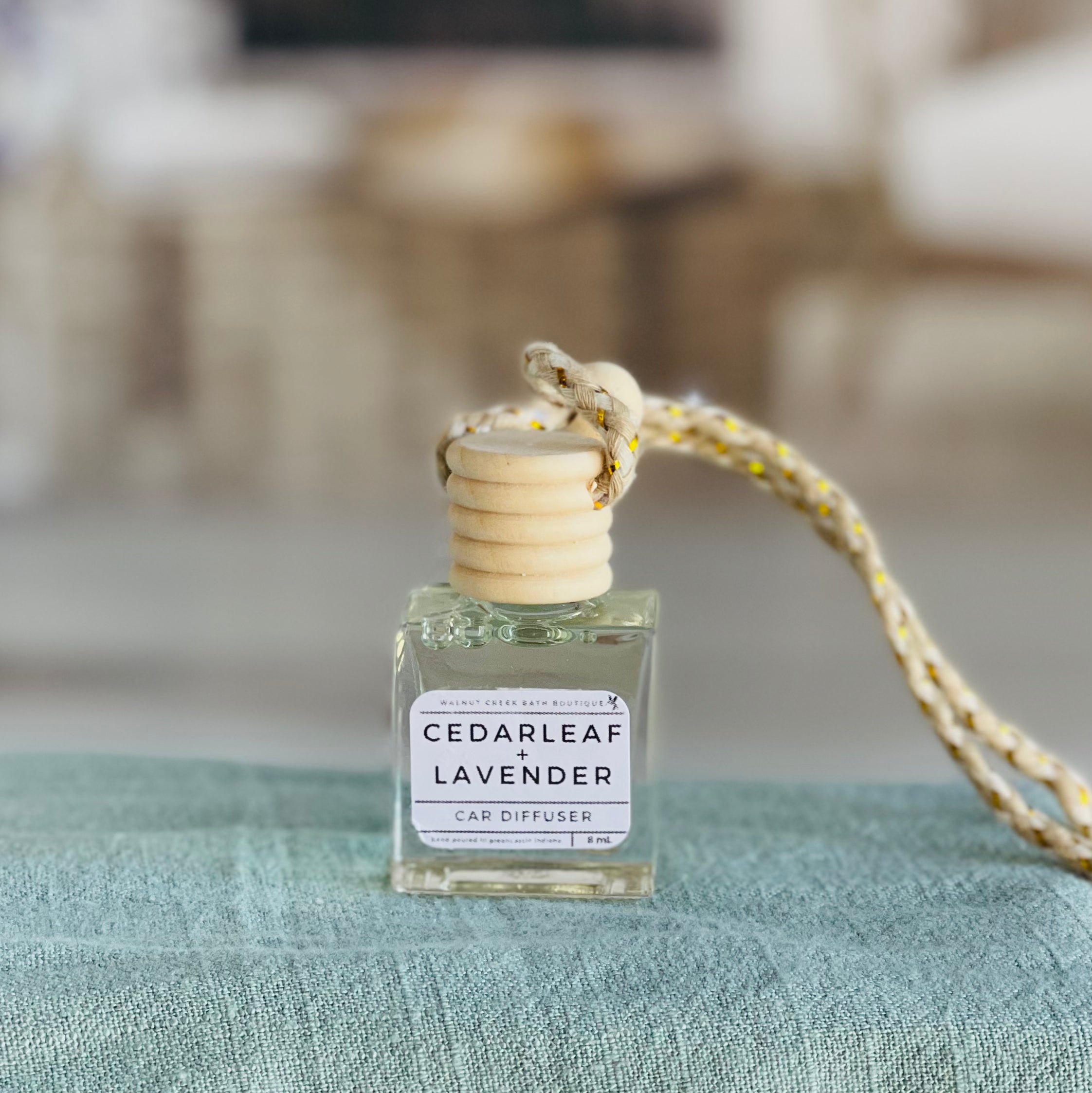 cedarleaf and lavender car diffuser shown up close on a green cloth in front of a wicker basket.