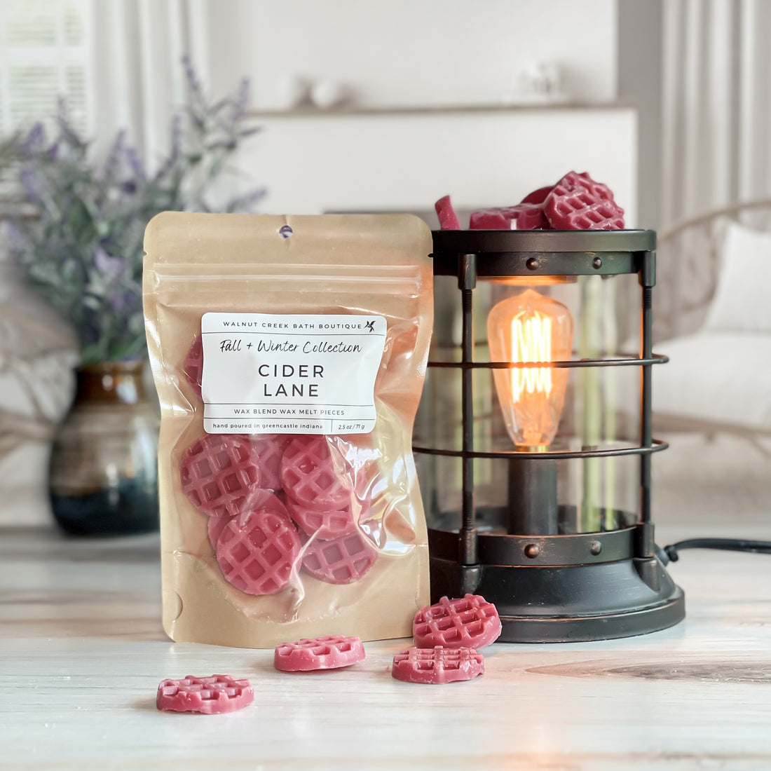 cider lane wax melt bag next to lit burner. there are wax melts on the table scattered about to shoe the pieces - these are red tiny waffle pieces