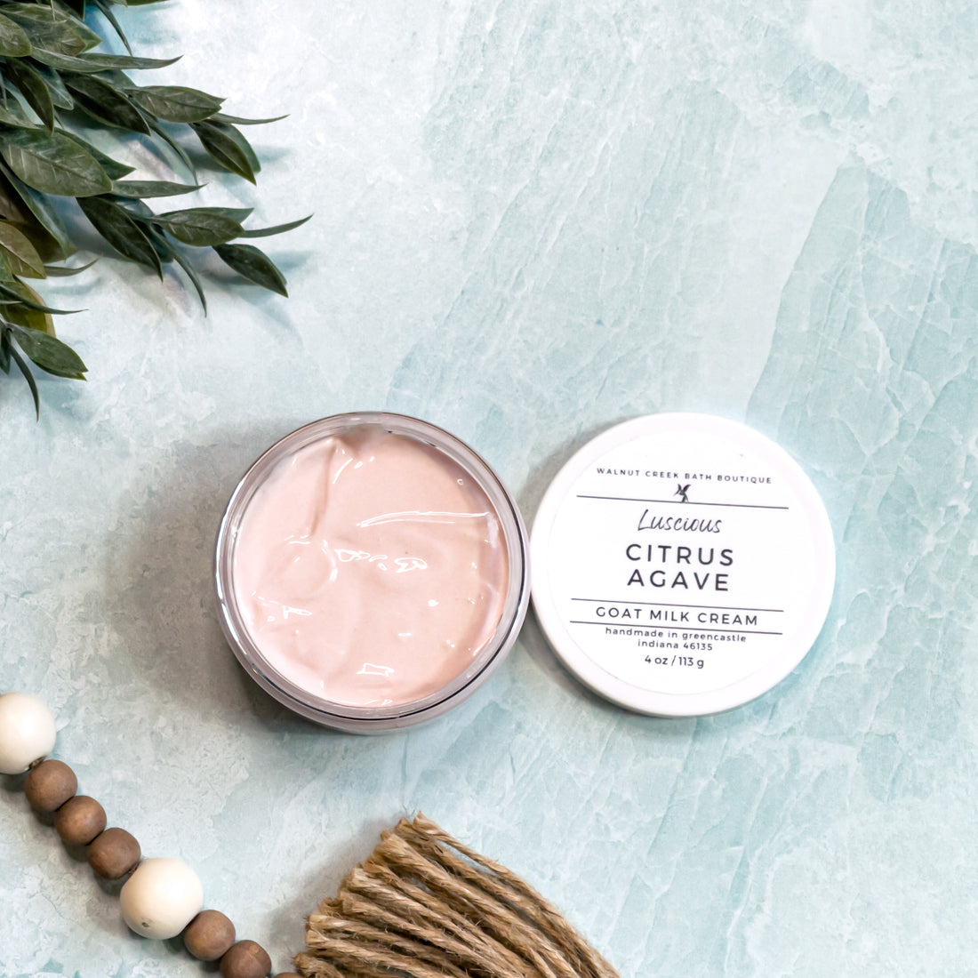 Two round containers of Citrus Agave Goat Milk Cream with white lids, labeled with the product name and branding on a marble surface.