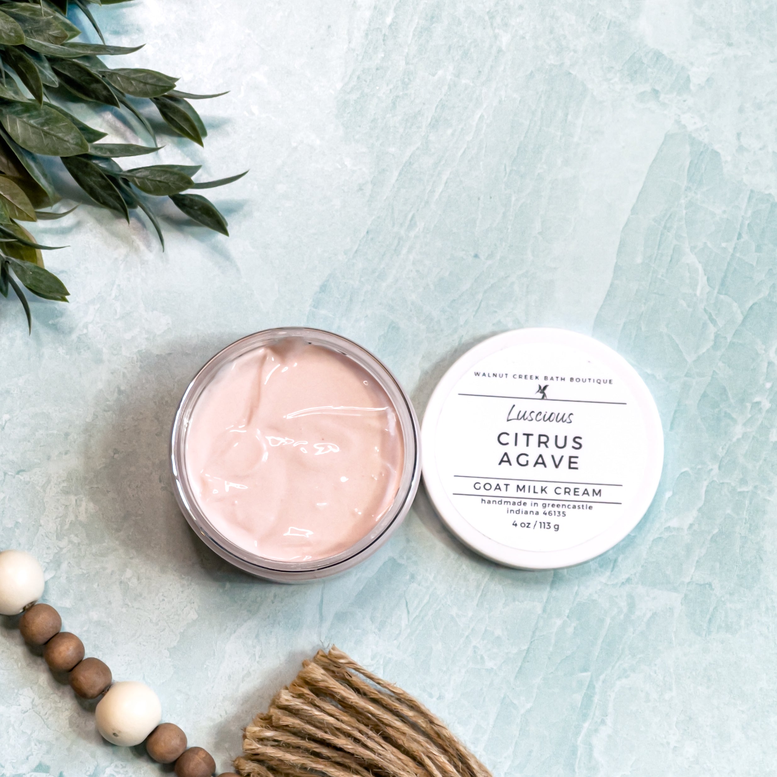 Two round containers of Citrus Agave Goat Milk Cream with white lids, labeled with the product name and branding on a marble surface.