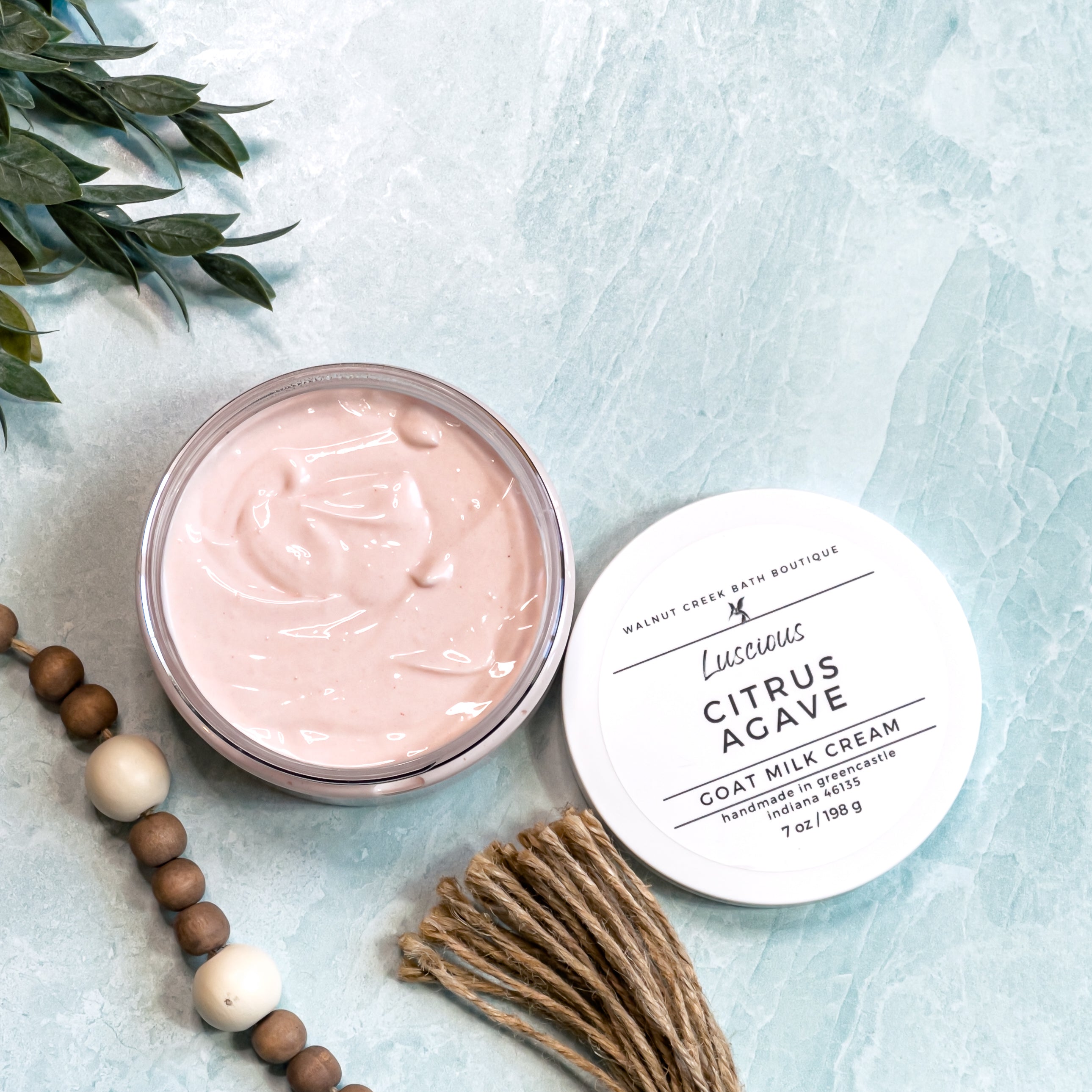 Two round containers of Citrus Agave Goat Milk Cream with white lids, labeled with the product name and branding on a marble surface.