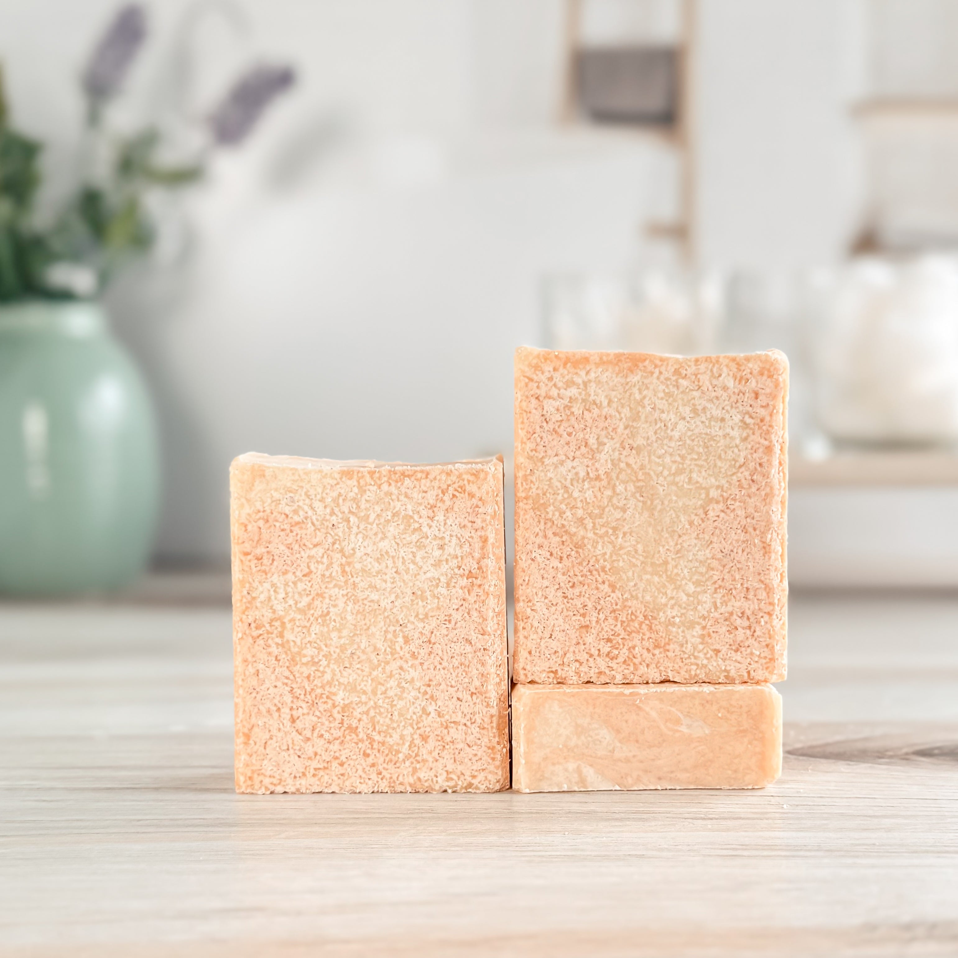 Three square beige bars of soap on a wooden surface with a blurred background