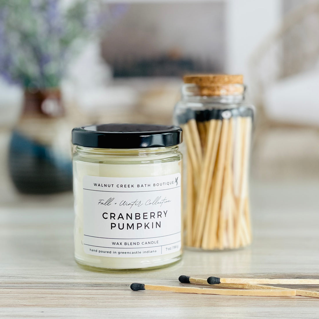 cranberry pumpkin candle with black lid. there are a few matches scattered in front and a pretty glass jar of matches in the background