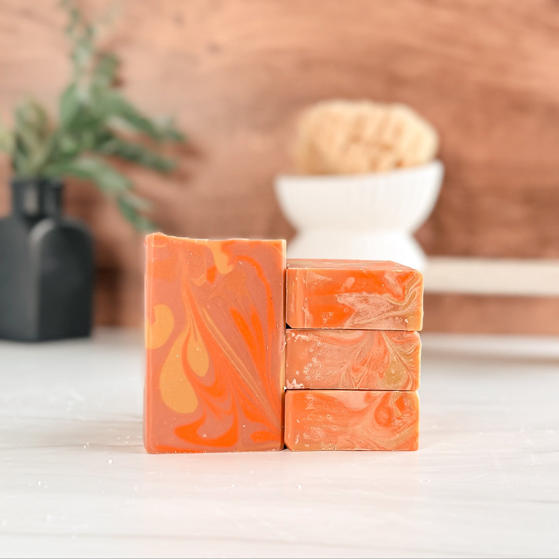 Stack of orange and green marbled soap bars on a white surface with a wooden background.