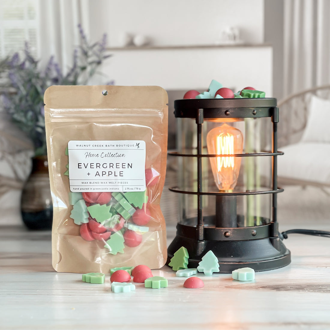 evergreen and apple wax melt bag next to lit burner. there are wax melts on the table scattered about to shoe the pieces - these are red dot pieces along with 2 colors of green tiny trees - so cute!