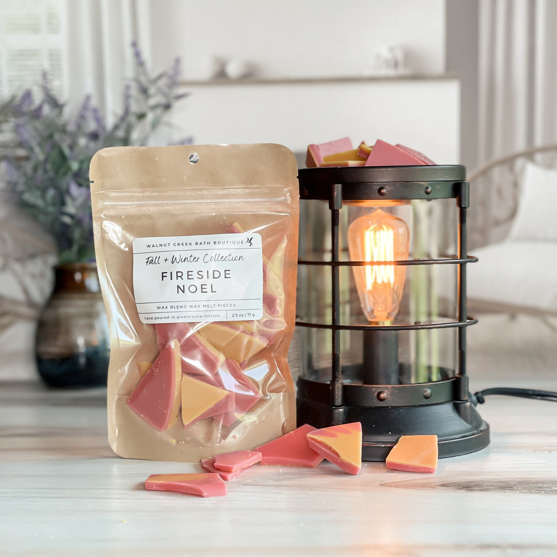 fireside noel wax melt bag next to lit burner. there are wax melts on the table scattered about to shoe the pieces - these are red and orange brittle pieces