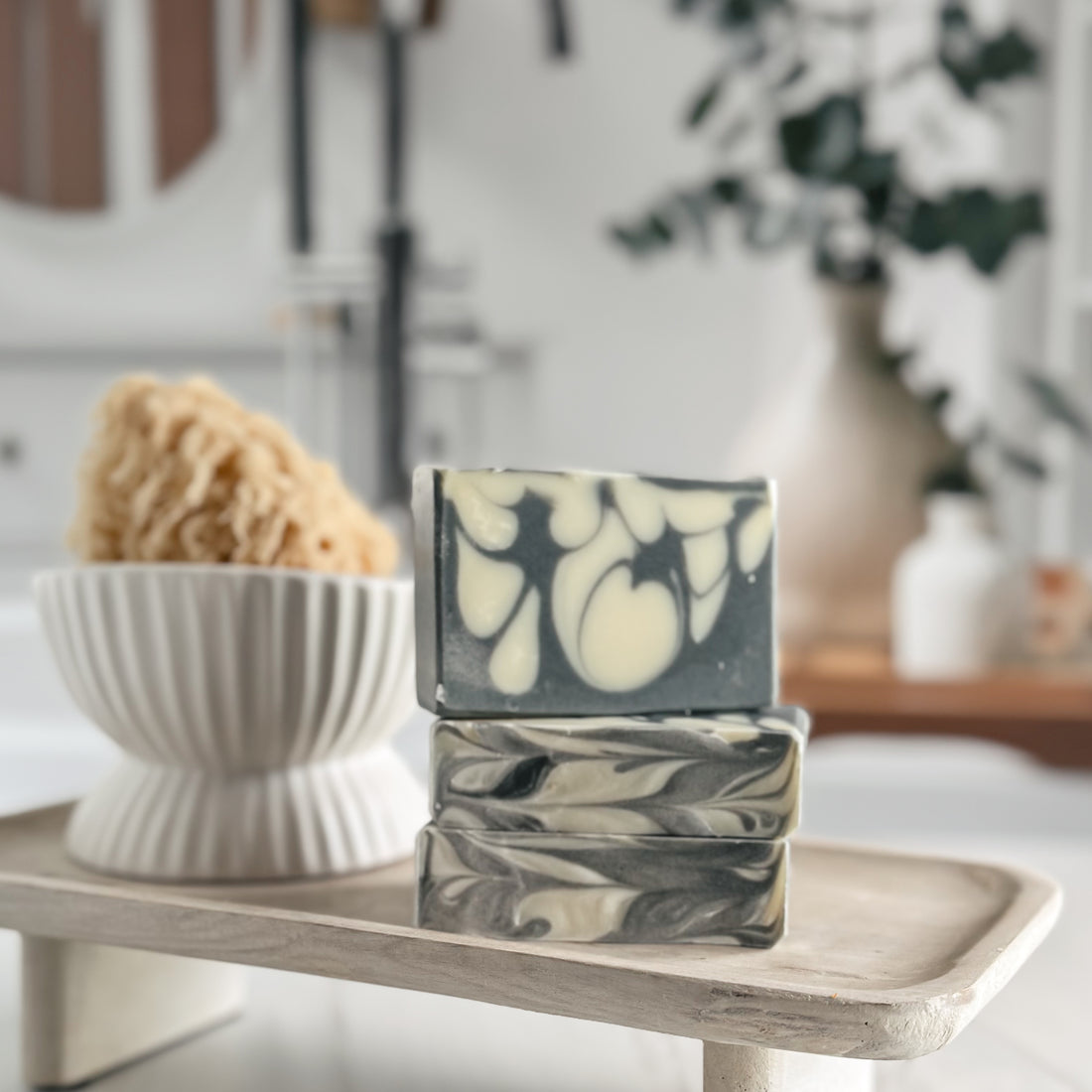 Stack of marbled soap bars on a wooden tray with a bowl and sponge in the background.
