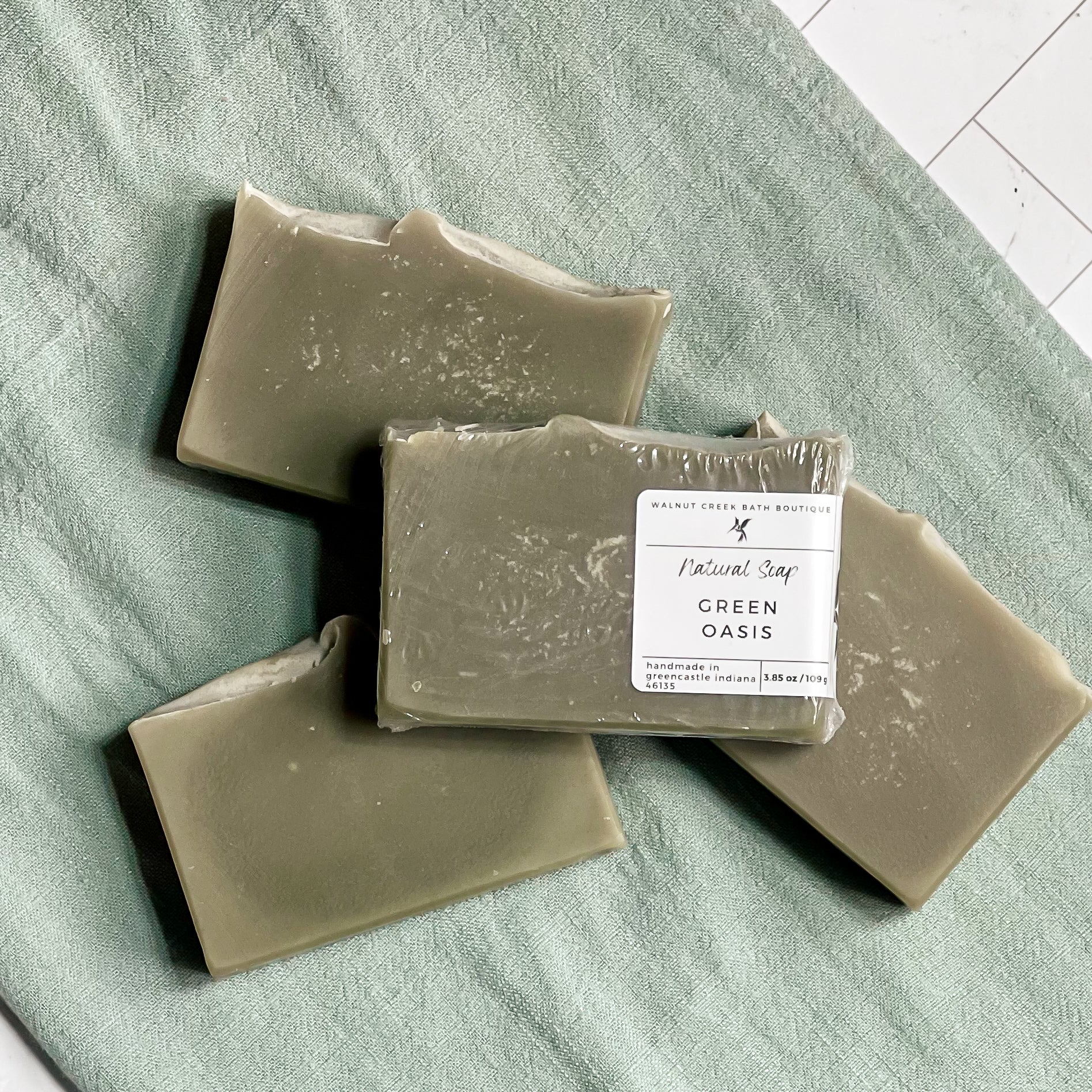 3 green oasis soaps are laying flat on a green cloth with another on top of them showing the label.