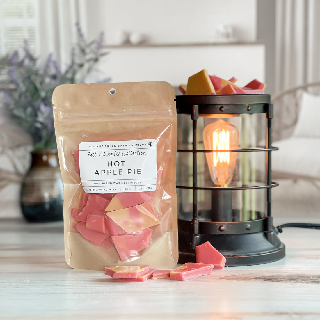 hot apple pie wax melt bag next to lit burner. there are wax melts on the table scattered about to shoe the pieces - these are red and orange brittle pieces