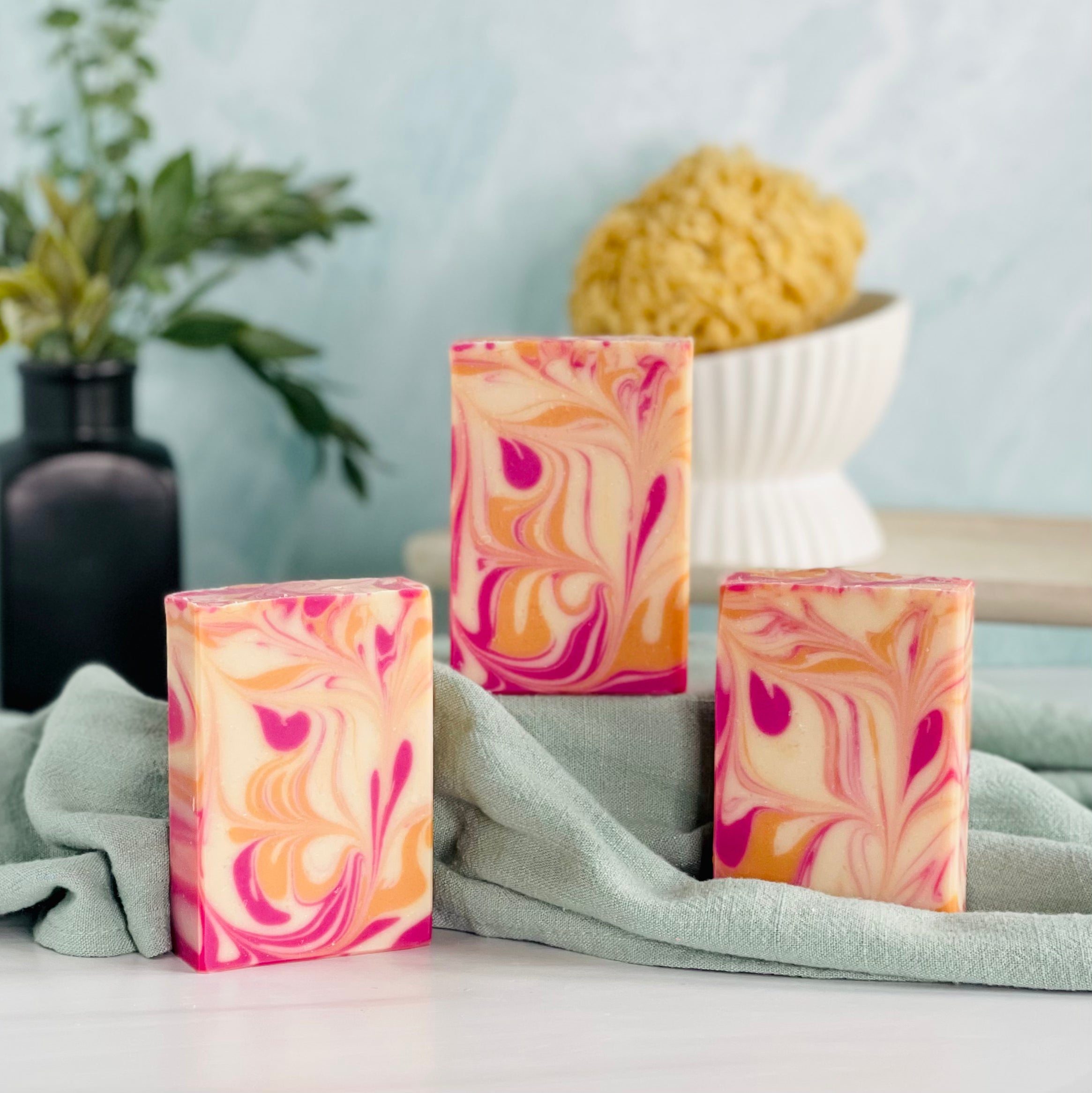 three lavender apricot soaps are shown with one on a green covered dias along with a loofah in a dish in the background