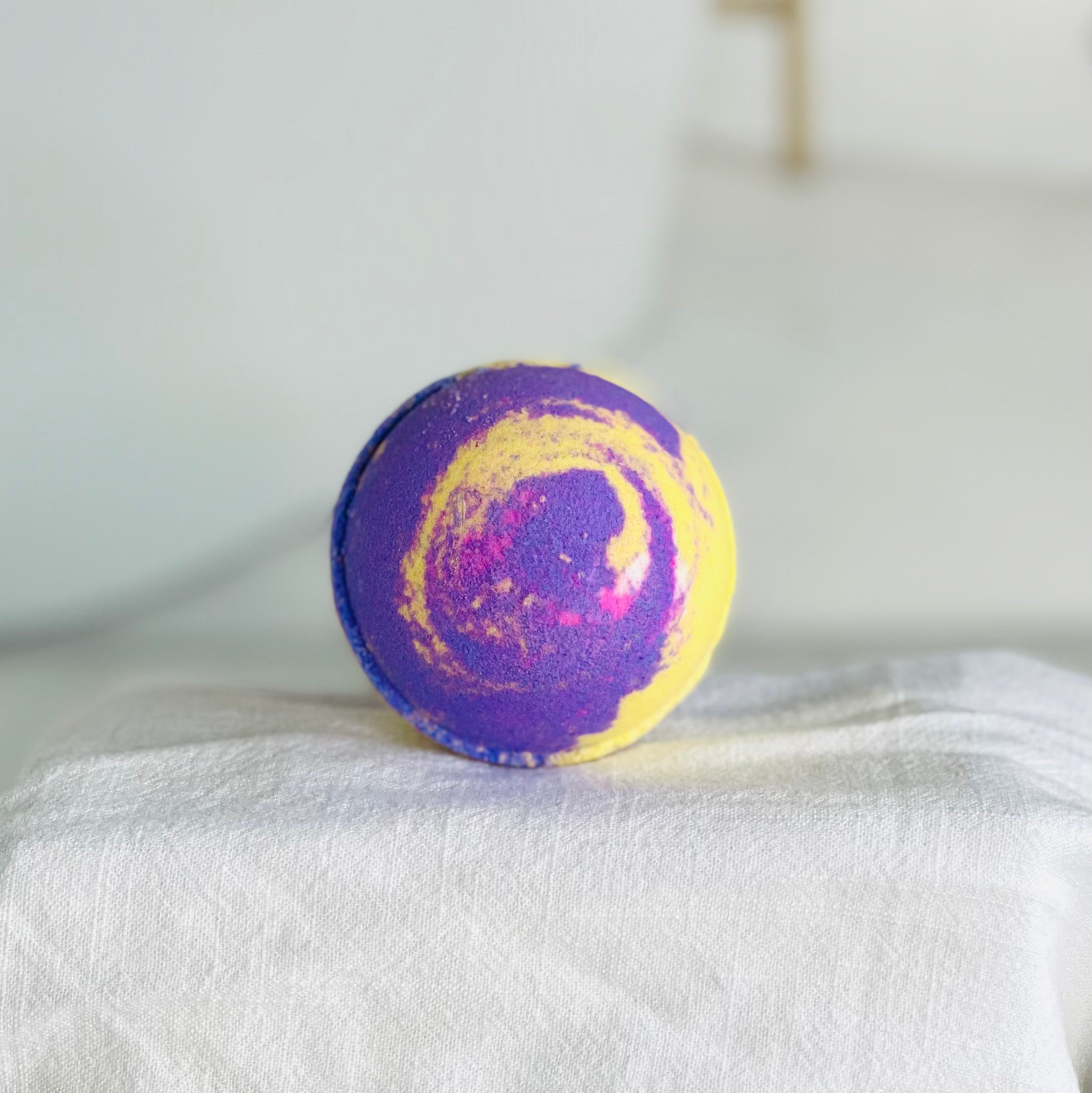 our lavender chamomile bath bomb has deep purple and deep yellow swirls. this is show best in this close up view of the bath bomb on a white cloth covered riser