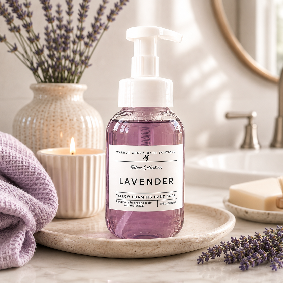 Lavender hand soap in a clear pump bottle with a white label, styled on a tray in a bathroom setting with lavender, a candle, and a towel.