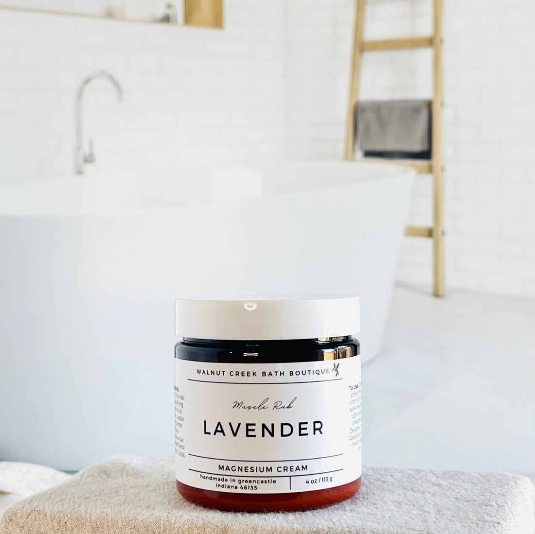 this magnesium cream is in an amber jar with a white lid is sitting on a raised platform in front of a spa lake bathroom. the label is simple white with black lettering