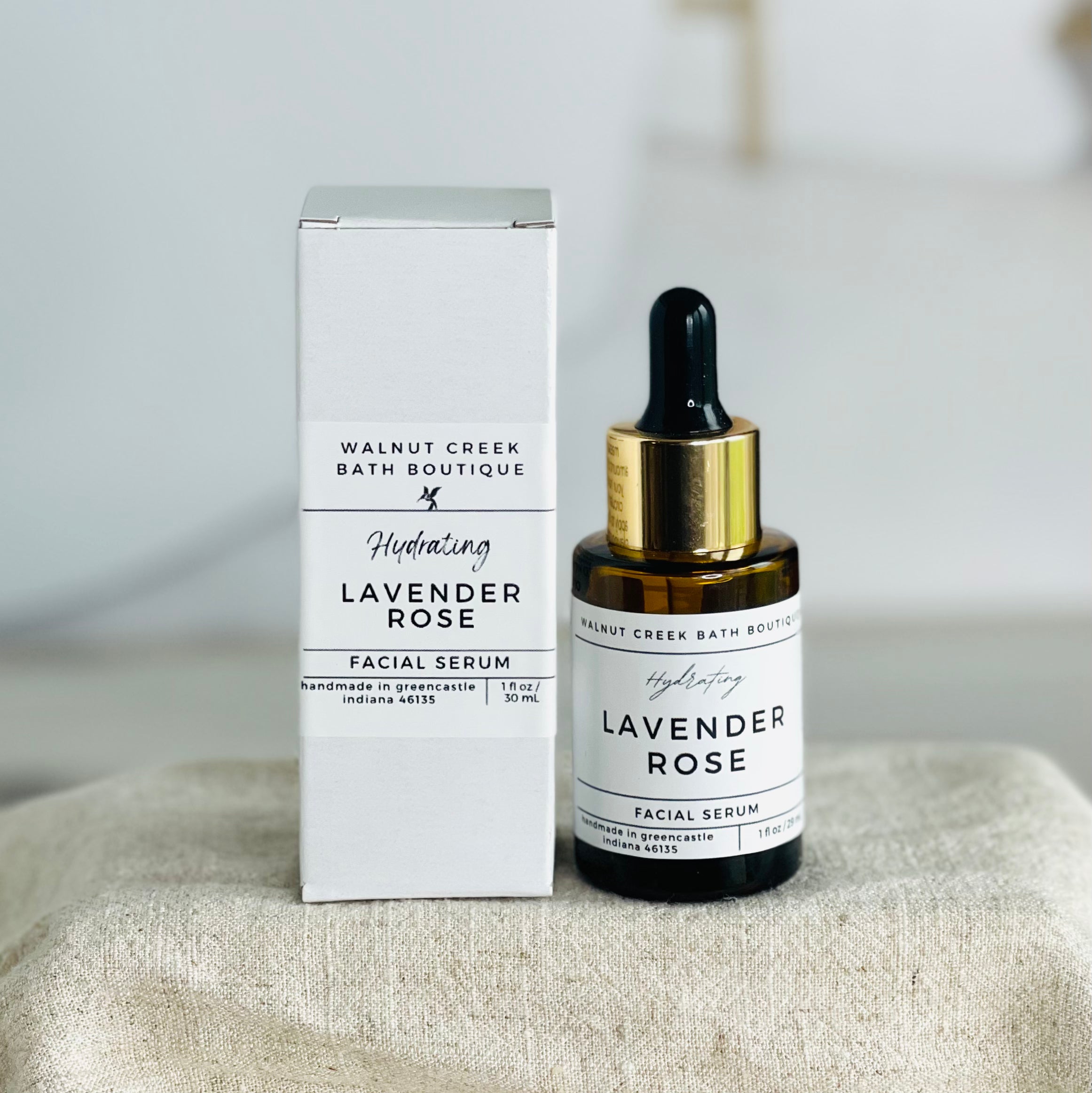 lavender rose facial serum in amber bottle with gold band next to white box
