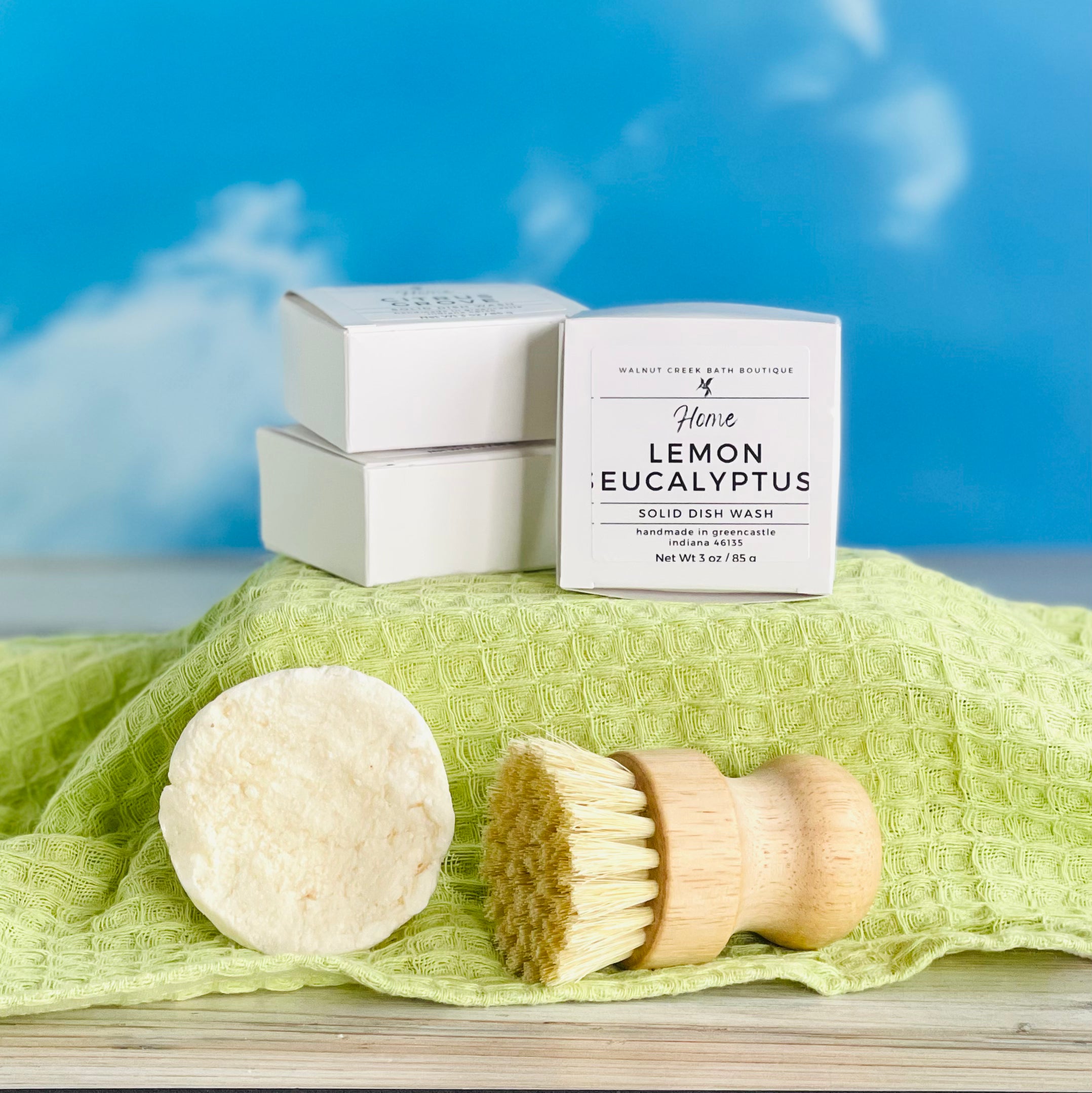 stacks of lemon eucalyptus dish wash refills on a green covered riser with an unboxed one with the brush below them