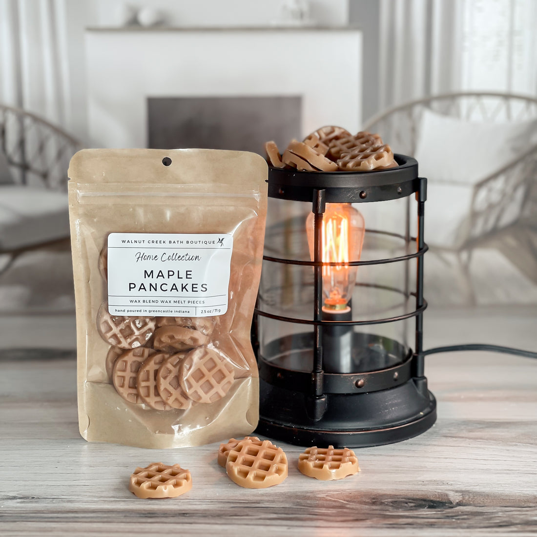 maple pancakes wax melt bag is full and standing next to a rustic farmhouse type burner that is on and filled with the pieces of wax in the shape of cute tan colored waffles. there are also a waffle pieces on the table in front of both to show the size and color of the pieces