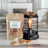 maple pancakes wax melt bag is full and standing next to a rustic farmhouse type burner that is on and filled with the pieces of wax in the shape of cute tan colored waffles. there are also a waffle pieces on the table in front of both to show the size and color of the pieces