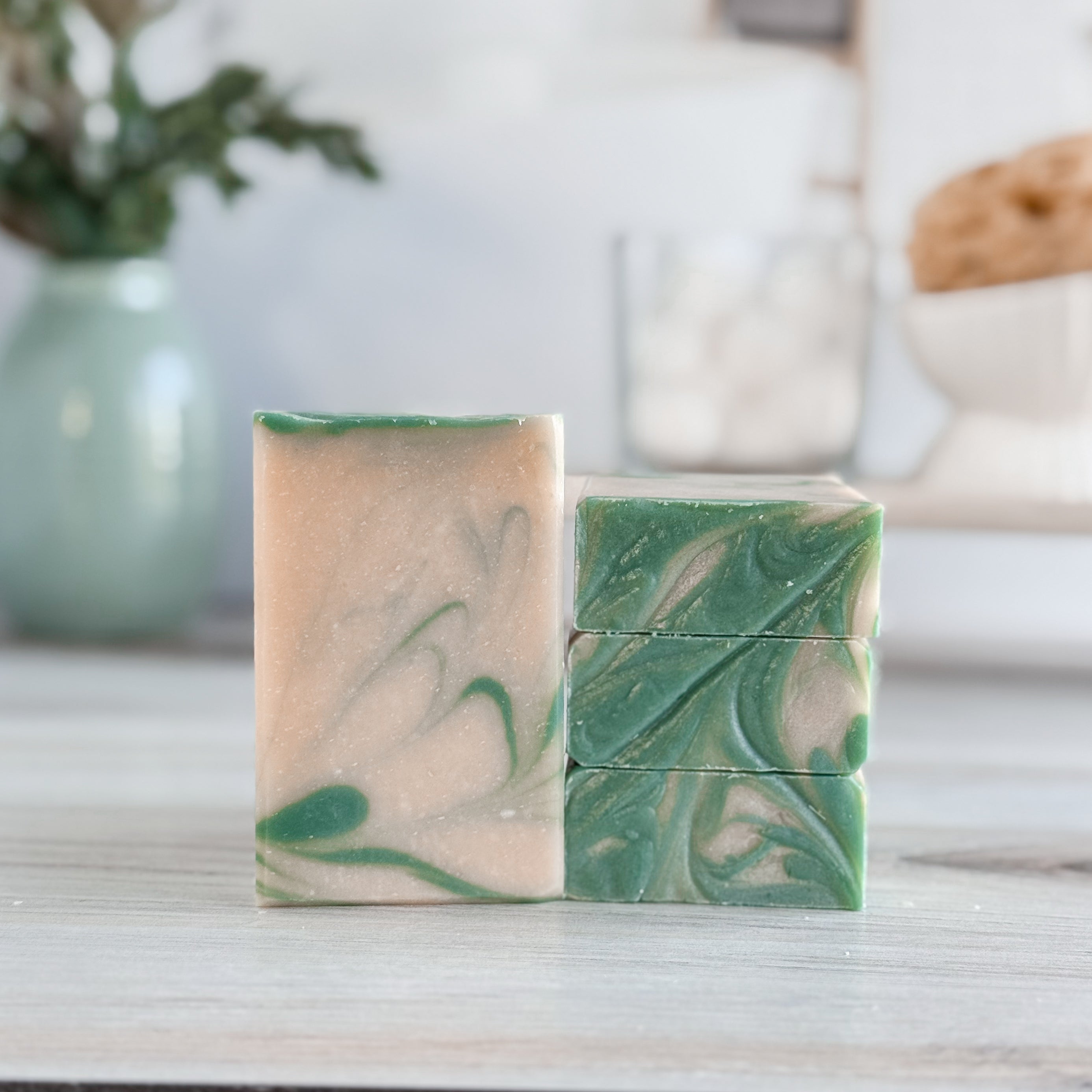 Two green and beige marbled soap bars on a wooden surface with a blurred background.