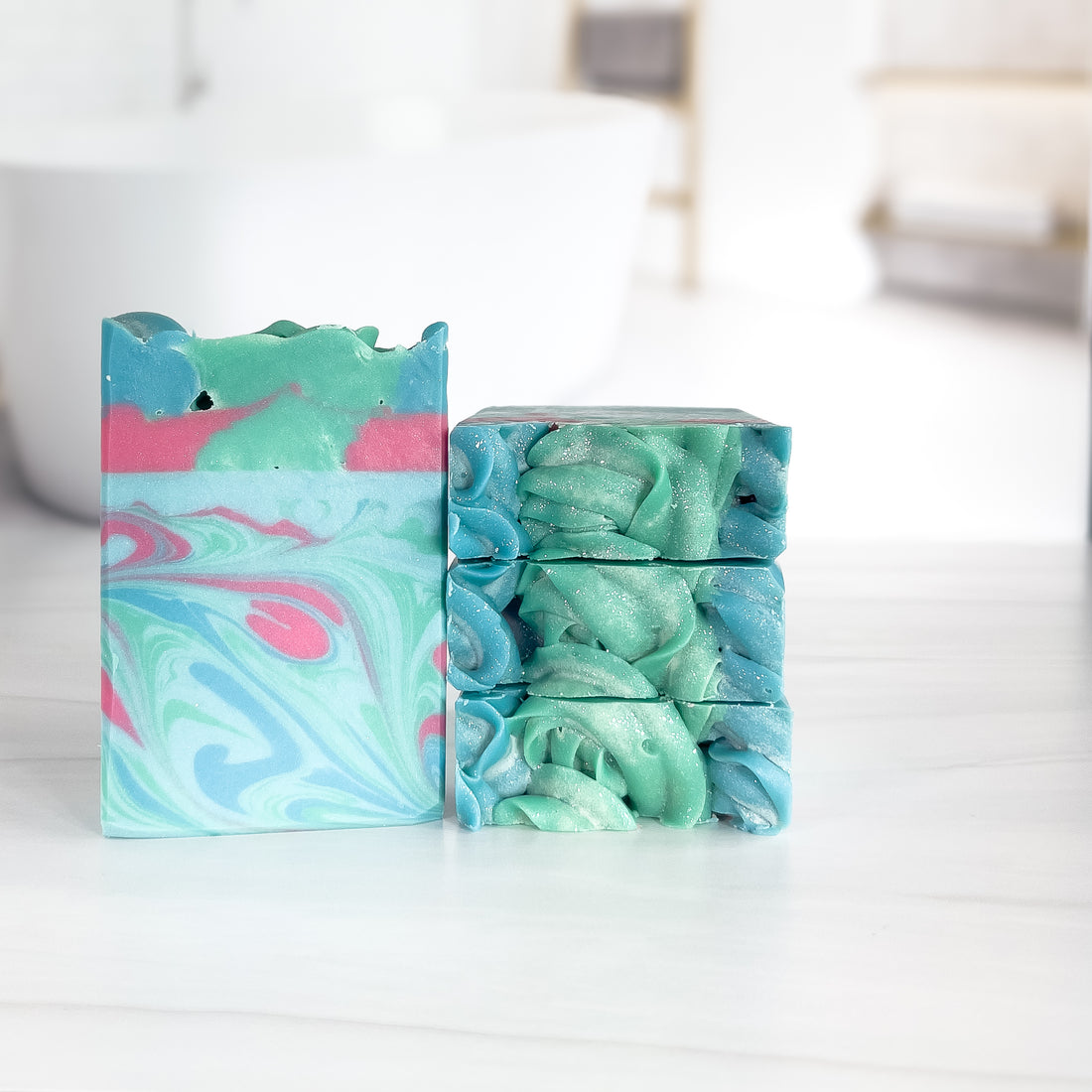 mermaid dreams soap is standing next to a stack of 3. the 3 show the fun top. the soap has mostly blue and green swirls with a touch of pink