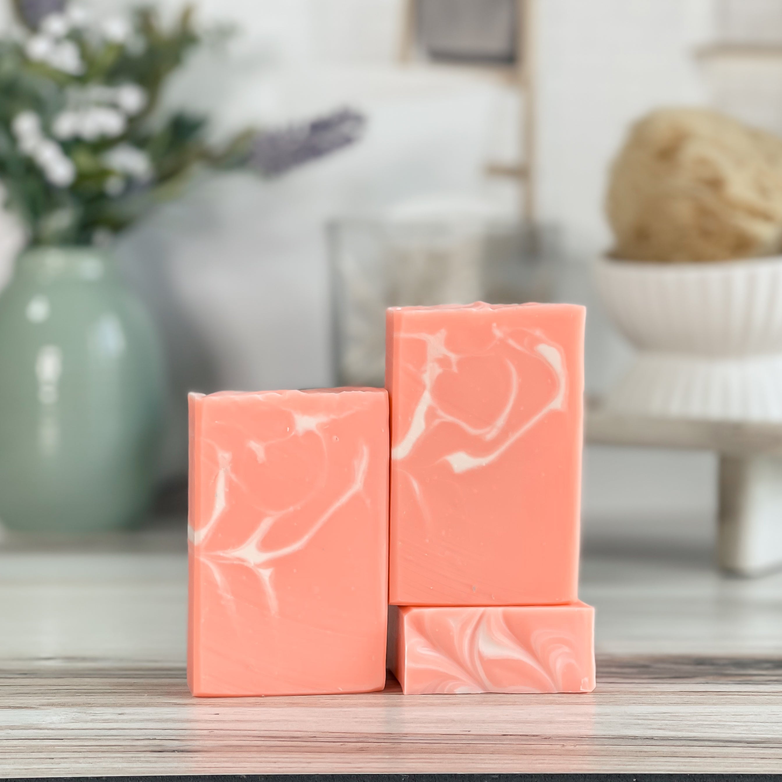 Three bars of peach colored soap with white marbling on a wooden surface, blurred background