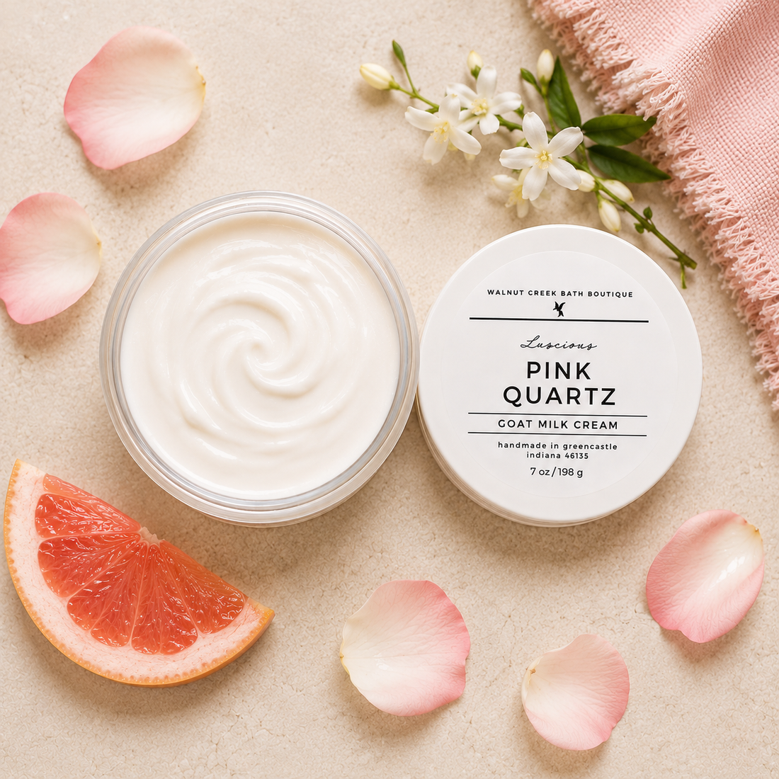 Goat milk cream jar with pink quartz label, surrounded by pink petals and a slice of grapefruit on a beige background.