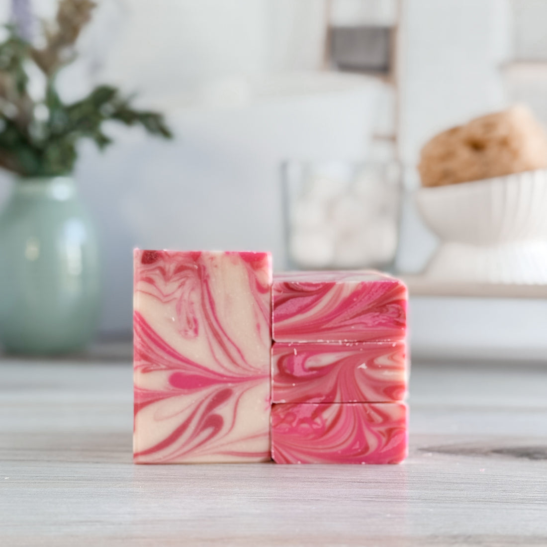 Two pink and white marbled soap bars on a wooden surface with a blurred indoor background.