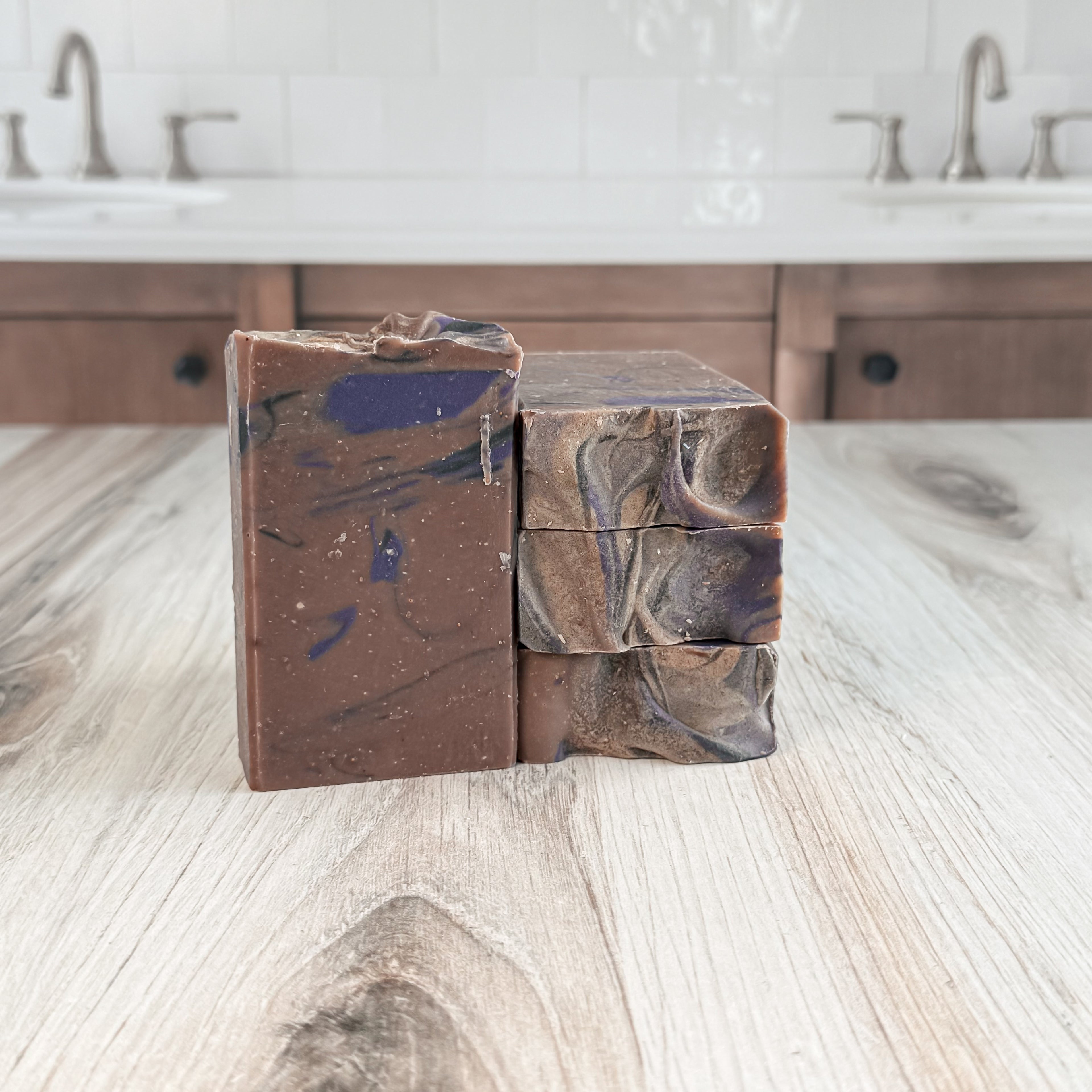 Three bars of brown soap with swirl patterns stacked on a wooden surface.