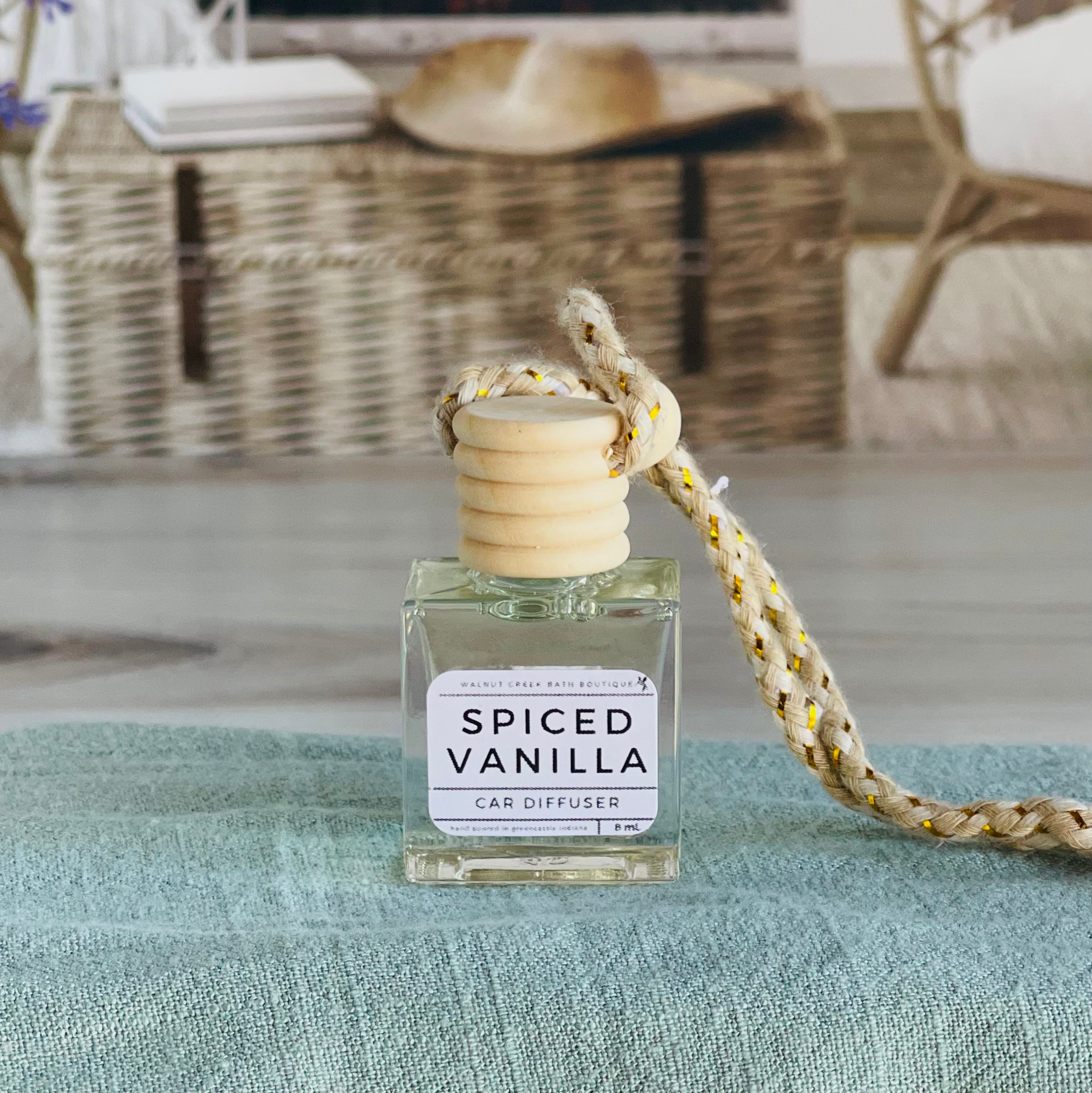 spiced vanilla car diffuser shown up close on a green cloth in front of a wicker basket.
