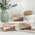 three stillwood soaps are shown with one on a tan covered dias along with a loofah in a dish in the background
