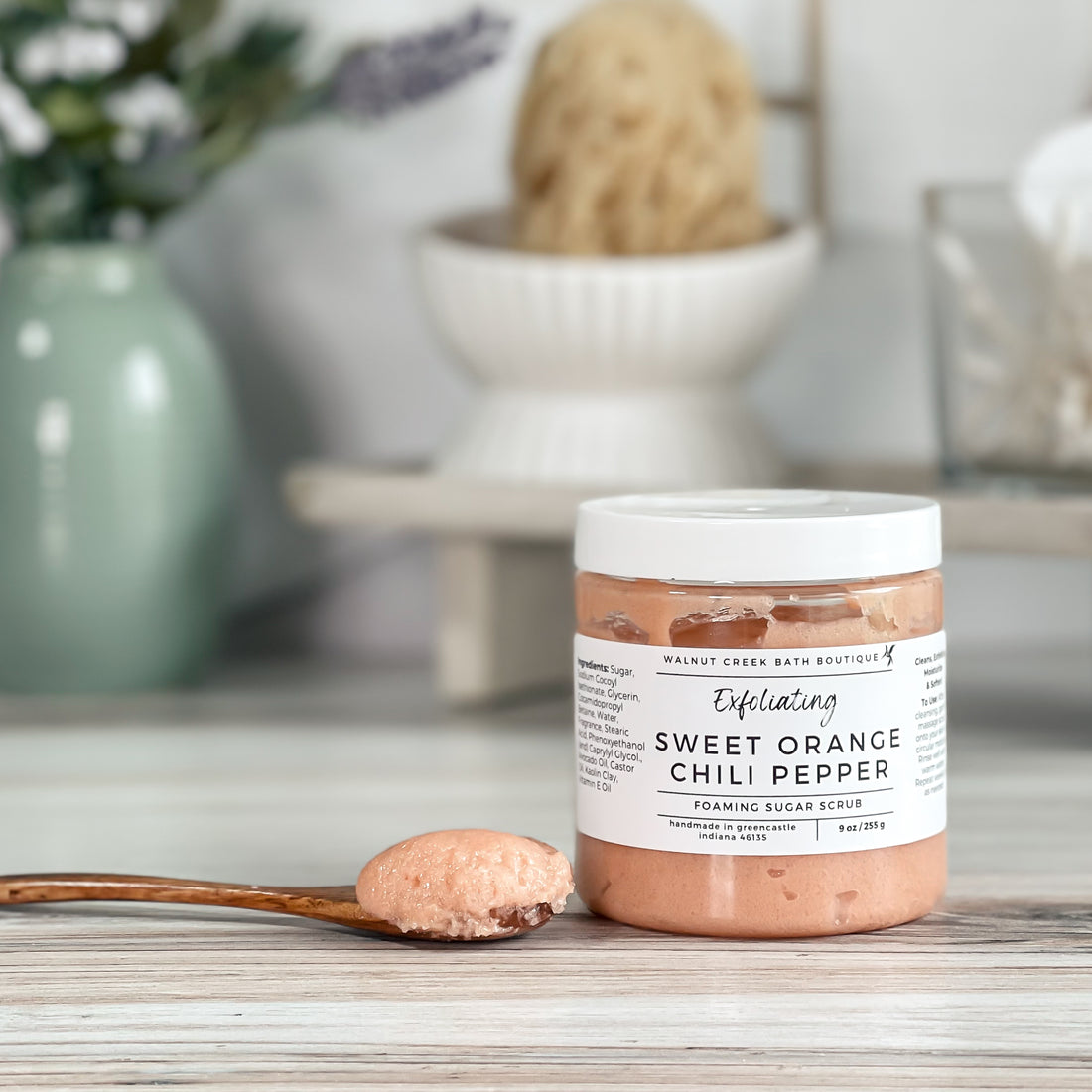 Jar of Sweet Orange Chili Pepper foaming sugar scrub with a spoonful of scrub on a wooden surface.