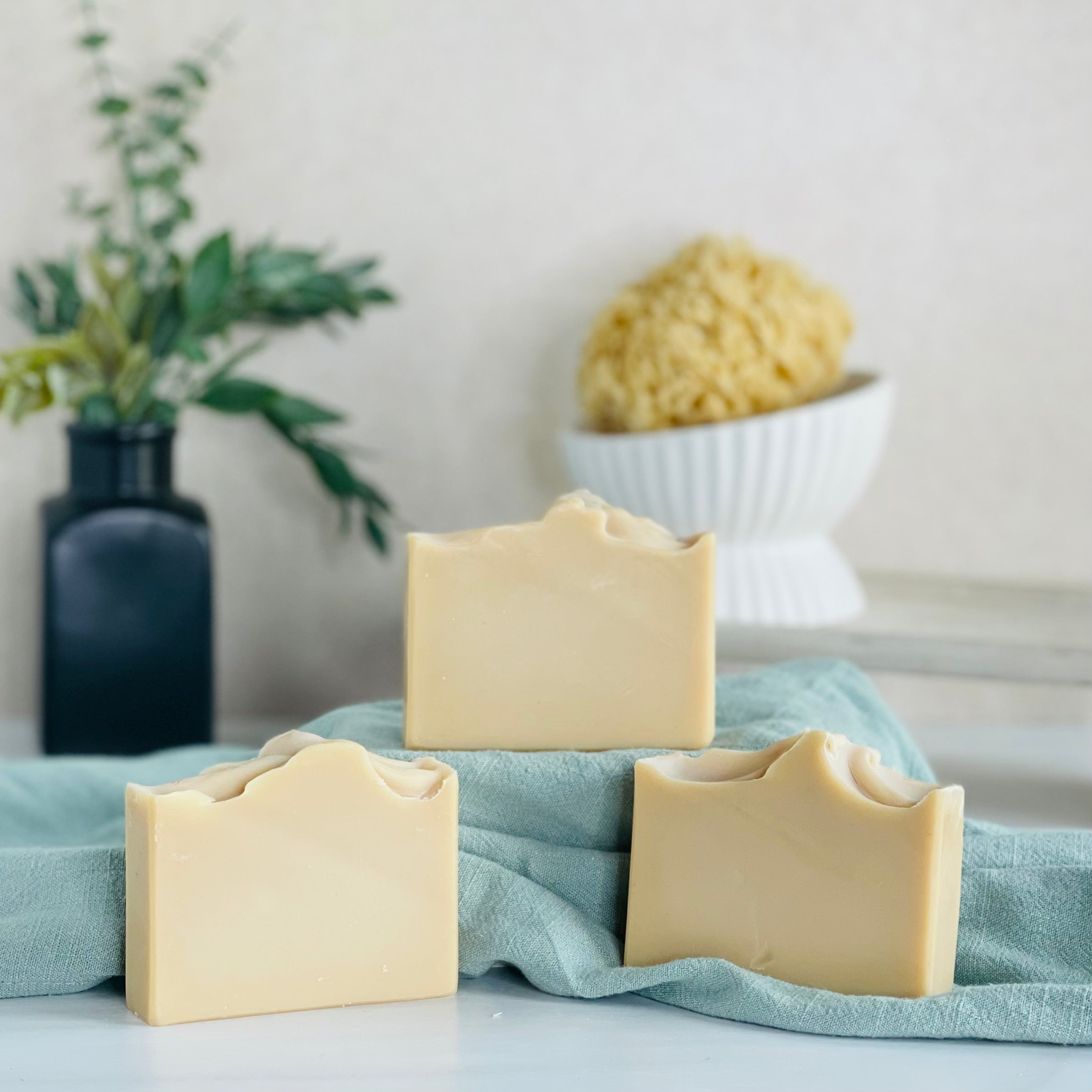 three patchouli sunrise soaps are shown with one on a sage green covered dias along with a loofah in a dish in the background