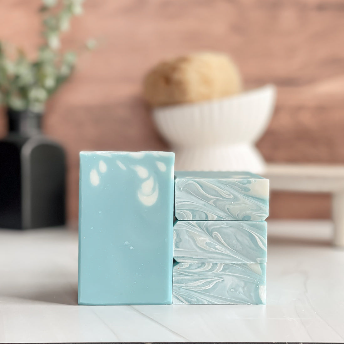 Two bars of light blue soap with white marbling on a white surface, blurred background