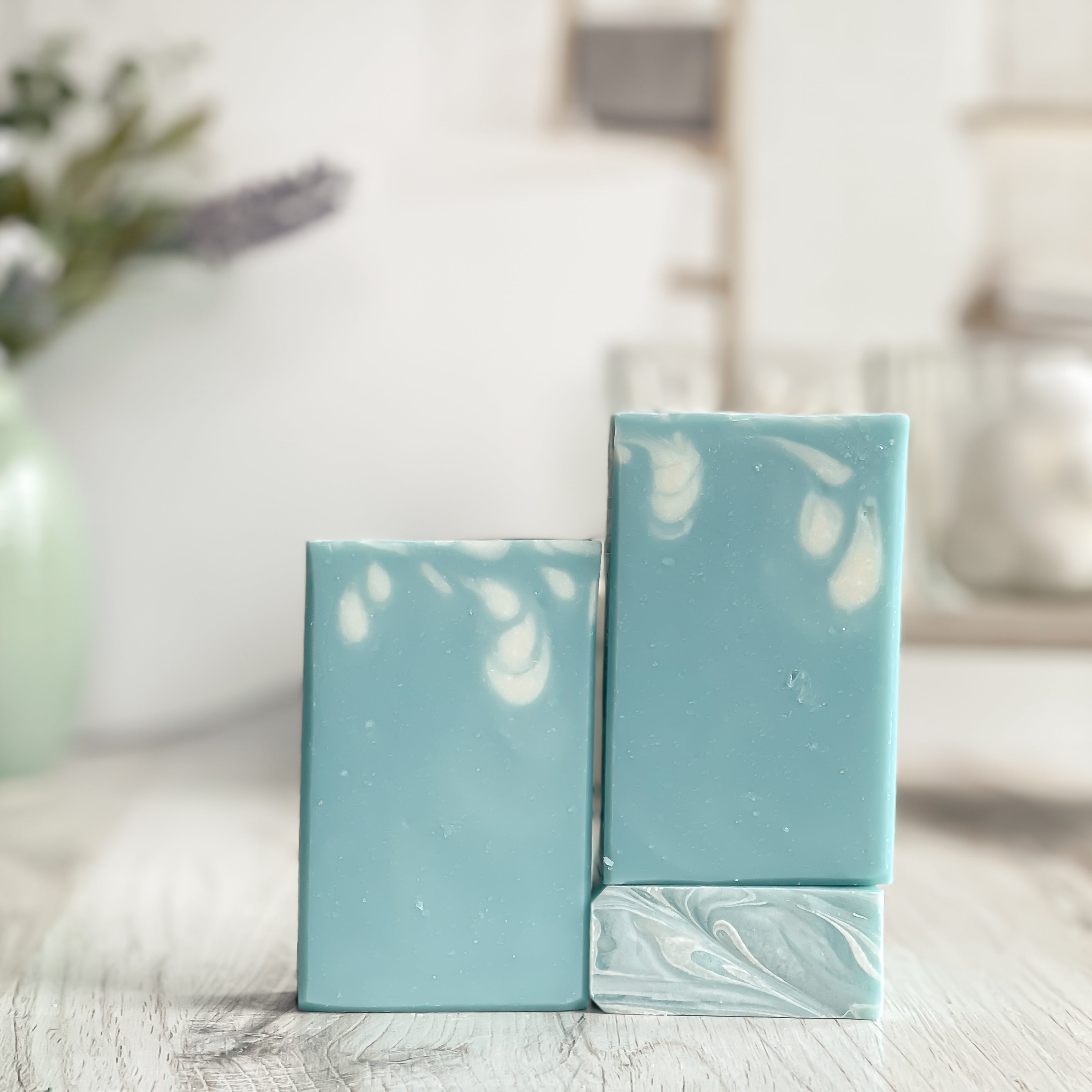 Two rectangular bars of light blue soap with white marbling on a wooden surface.