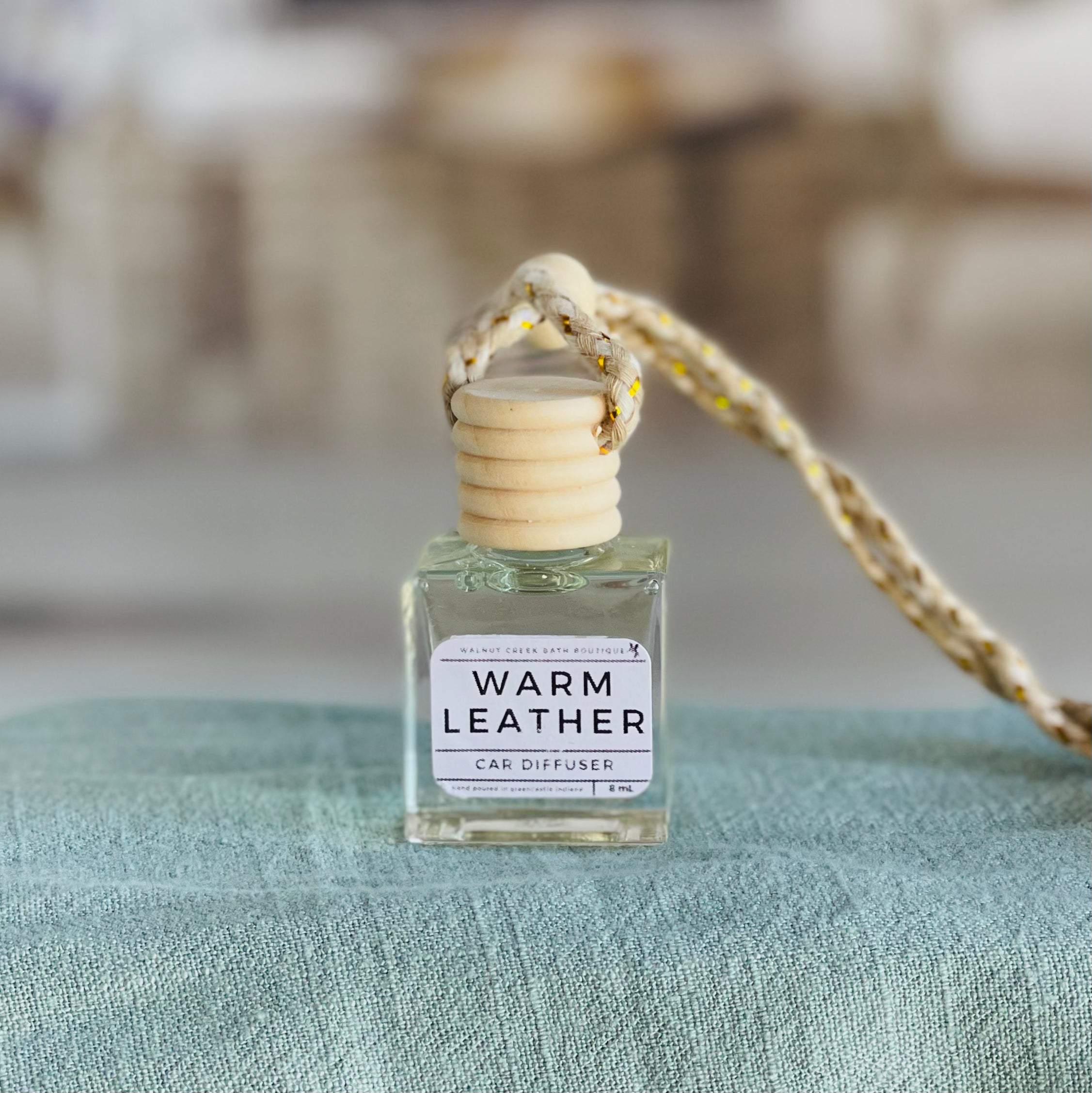warm leather car diffuser shown up close on a green cloth in front of a wicker basket.