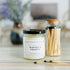 winters hearth candle with black lid. there are a few matches scattered in front and a pretty glass jar of matches in the background