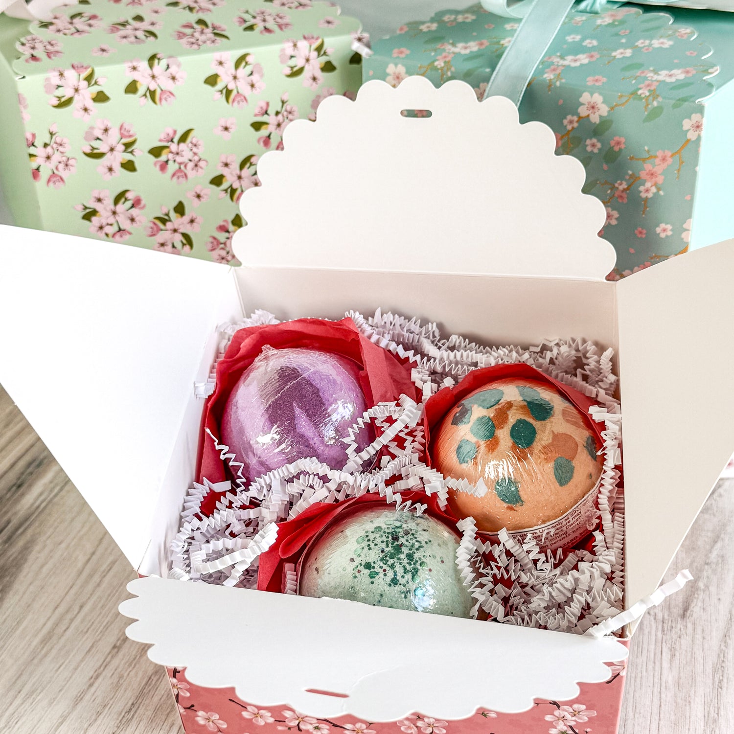 Three bath bombs in a decorative box with floral wrapping paper in the background