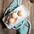 3 mango papaya bath bombs are shown sitting on a tray. two are in a soap dish in the shape of a turtle. there is a warm wood base and a green towel with white beads running under the tray and through the picture.