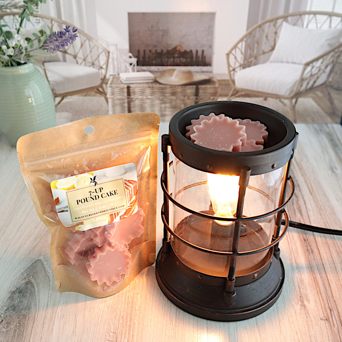 7 up pound cake wax melts are in a bag standing next to a lit burner. the burner has some of the starburst shaped wax melts in it getting ready to be melted. this is all sitting on a washed out wooden base with a couple of chairs in the background next to a fireplace
